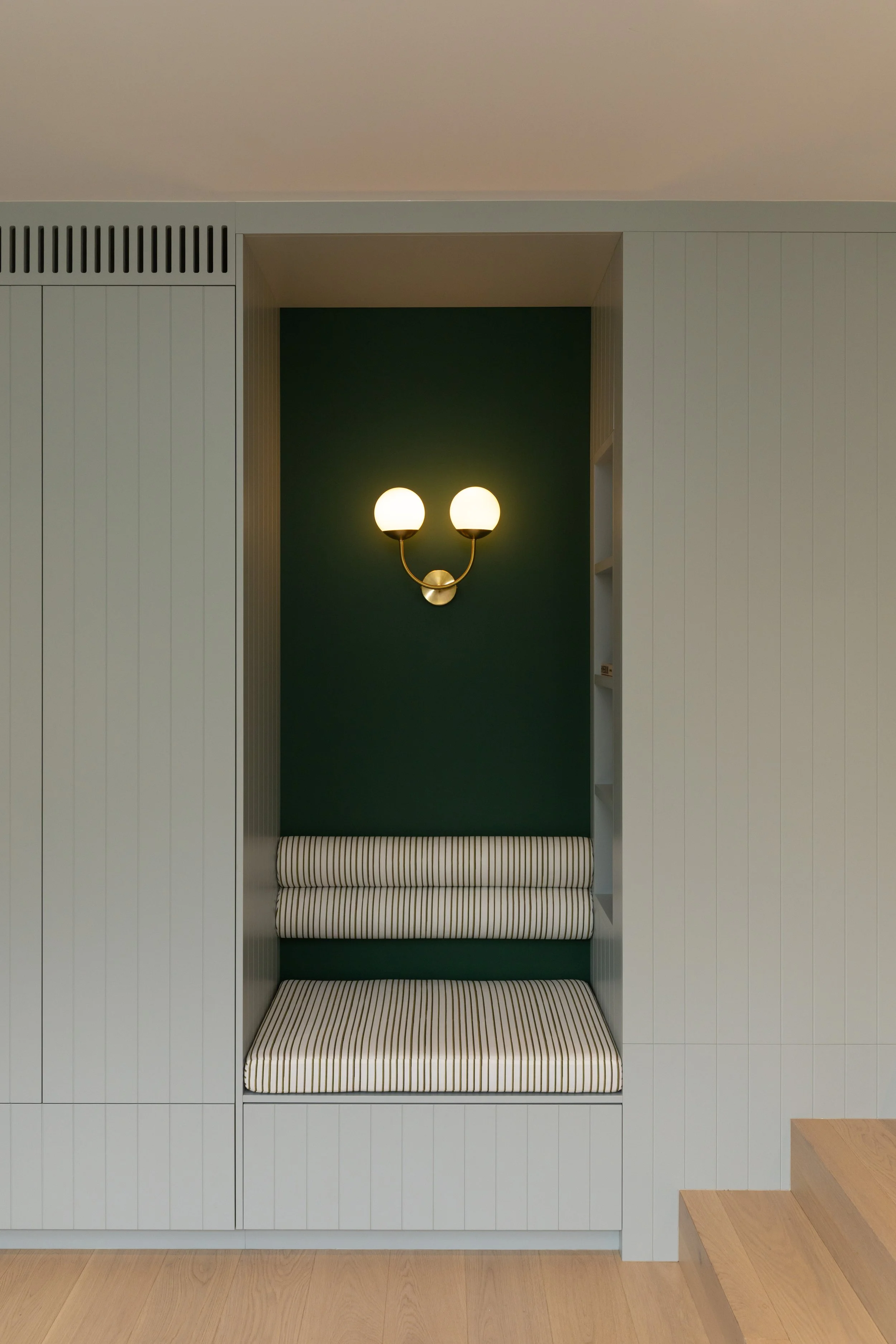Built-in seating nook with green back wall, striped cushion and a double bulb wall sconce.