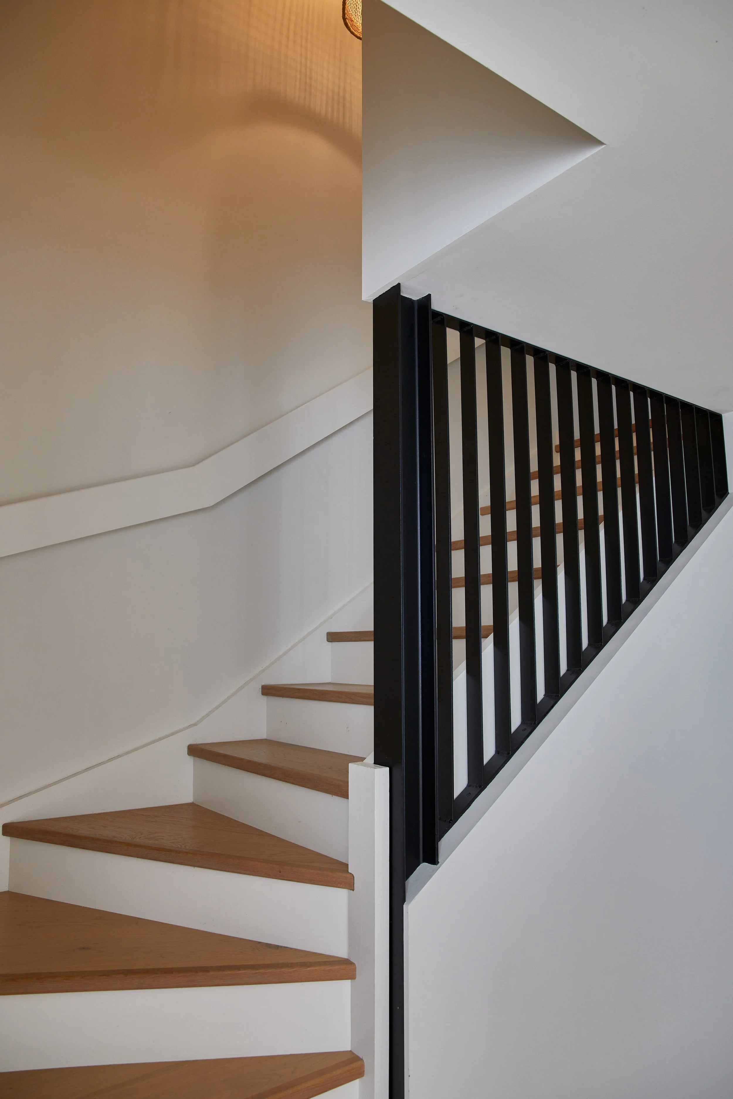 Interior staircase with wooden steps and black metal railing, viewed from the bottom looking up.