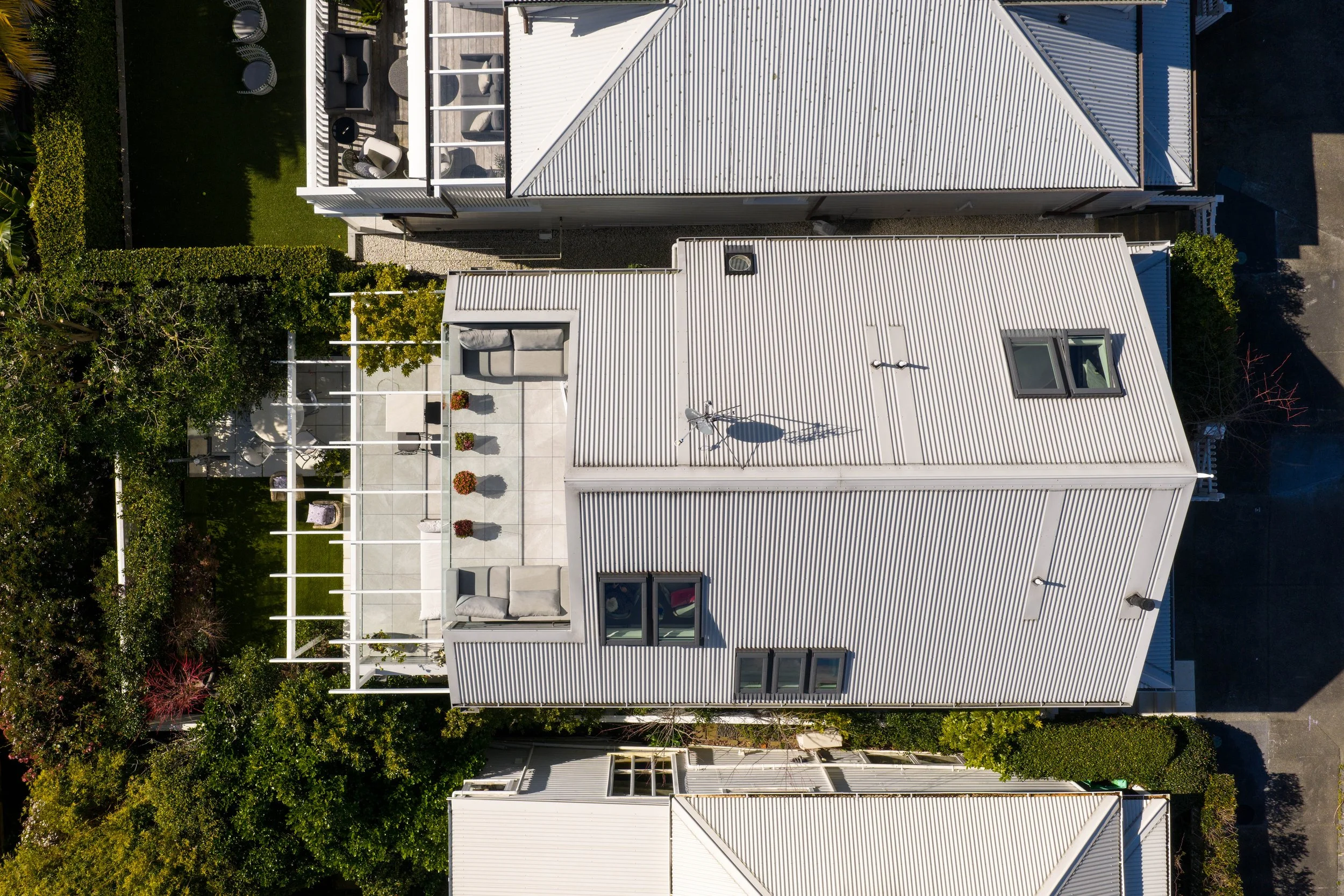 Aerial view of a modern house with a rooftop terrace, outdoor furniture, potted plants, and surrounding greenery.