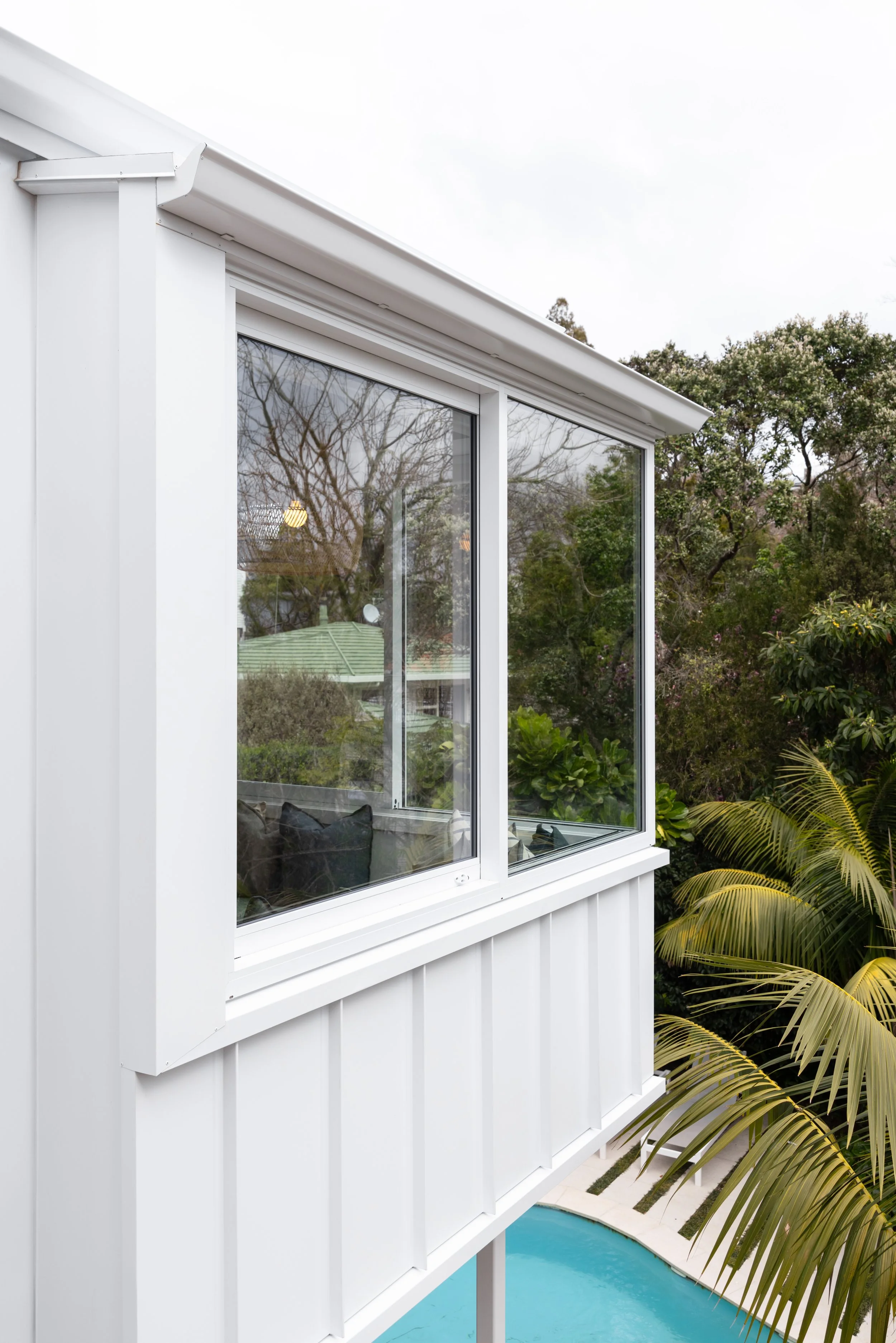 Close-up of a white balcony with large glass windows overlooking a garden and pool.