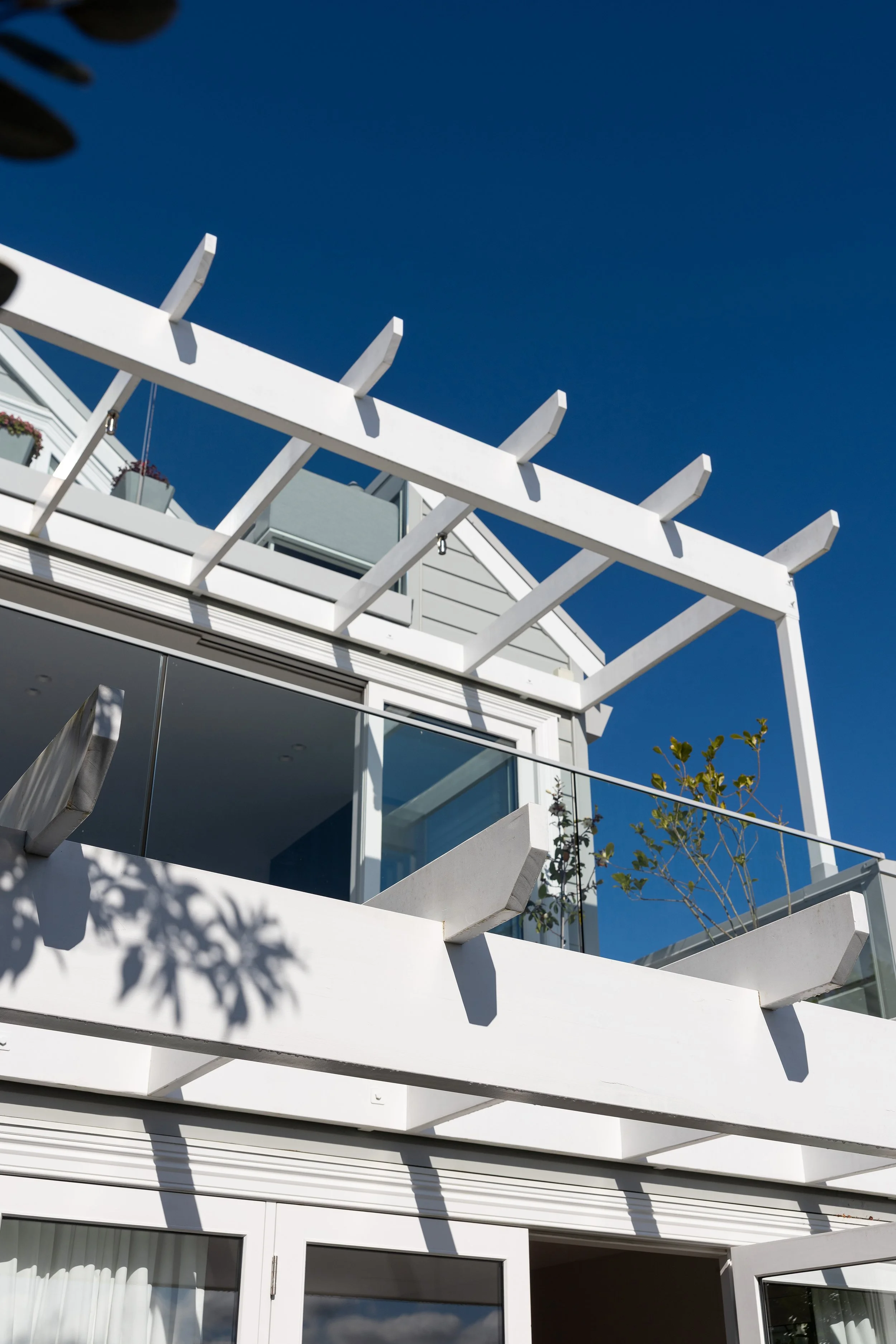 Modern white balcony with glass railing and potted plants, under a clear blue sky.