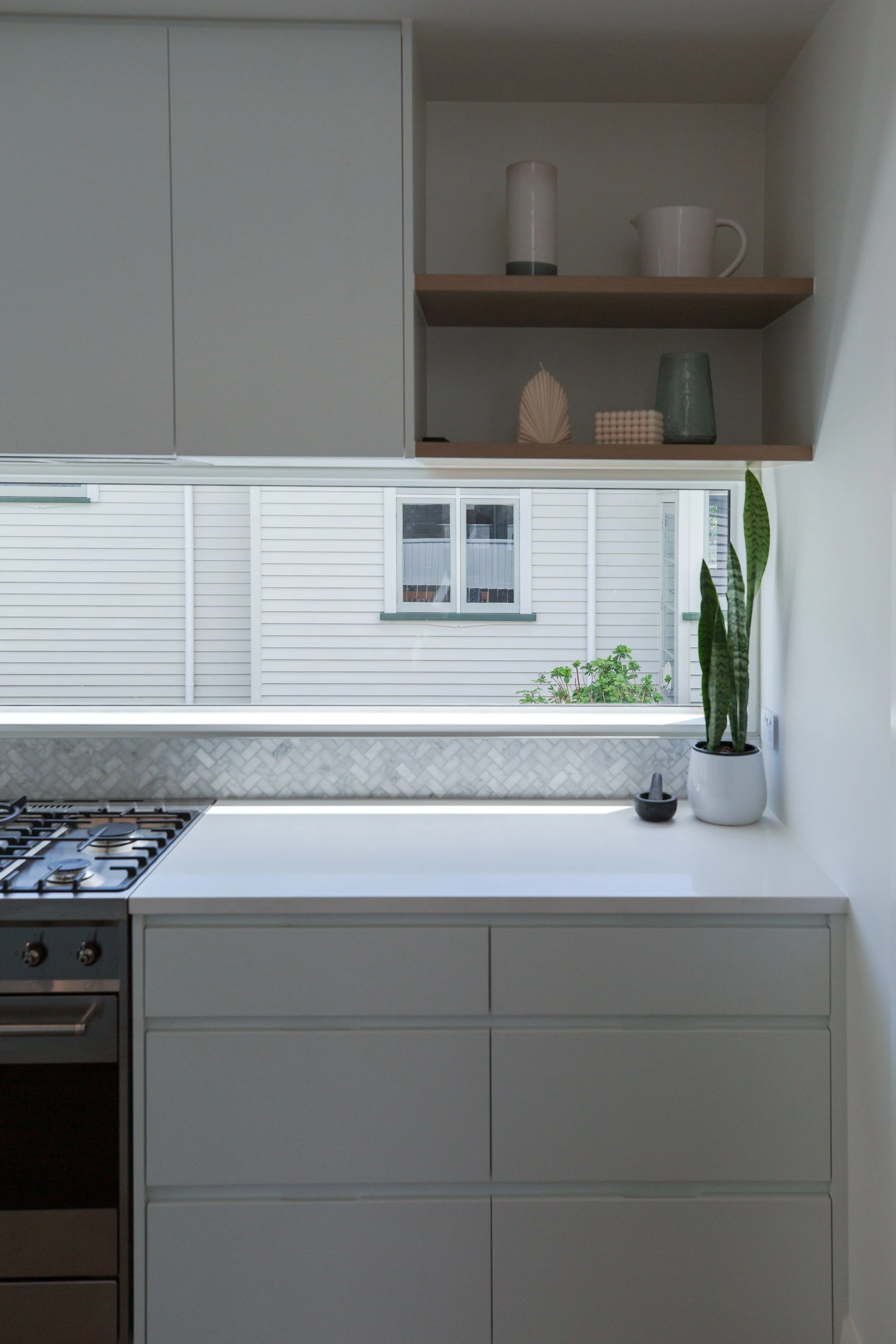 Modern kitchen with white cabinets, a window showing a fence and house outside, and a potted snake plant on the counter.