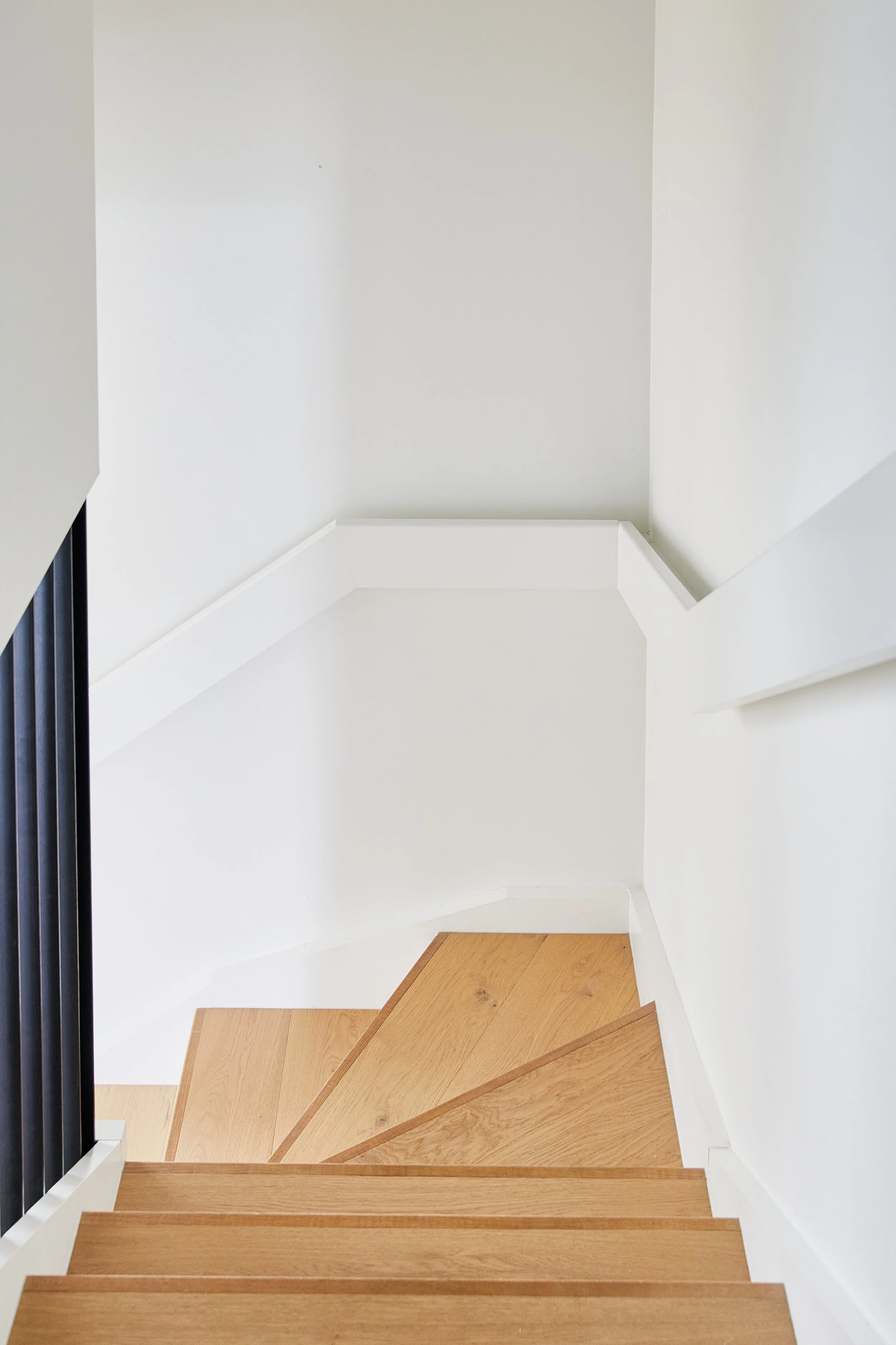 View of a staircase with wooden steps and white walls, featuring a black railing on the left side.