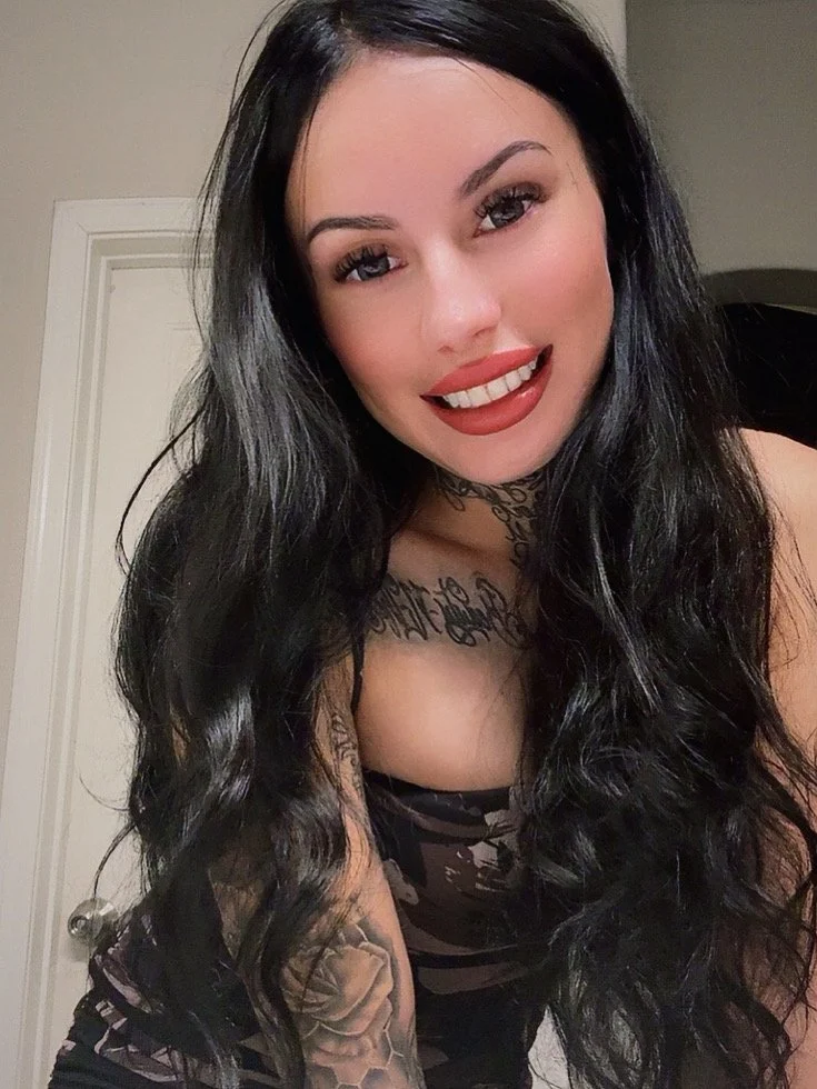 A woman with long black hair, fair skin, and wearing makeup, smiling and looking at the camera.