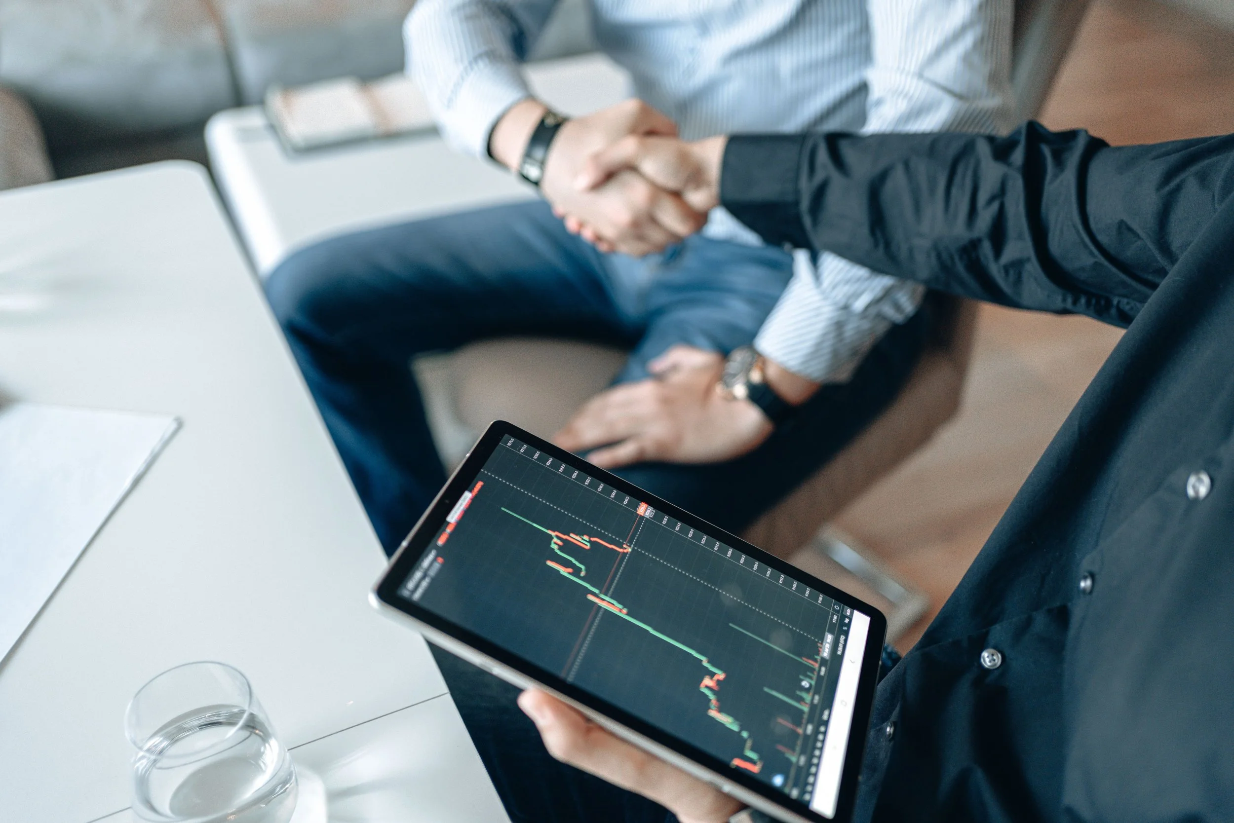 Person holding a tablet displaying financial stock charts with candlestick patterns in a business meeting.