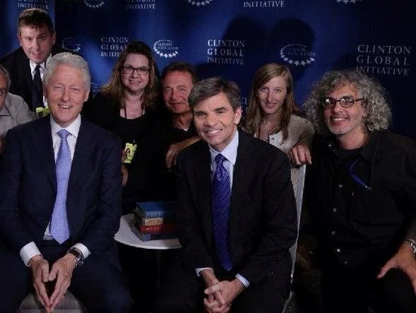 A group of seven people, including several men and women, smiling and posing together at a Clinton Global Initiative event, with a blue backdrop featuring the event's logo.