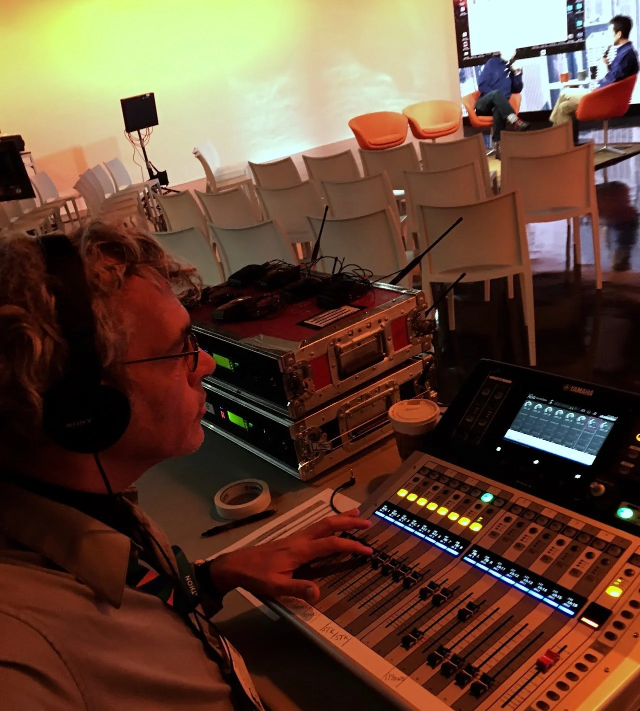 A person wearing headphones operating a sound mixing console and electronic equipment in a dimly lit venue.