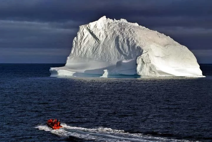 An iceberg floating in the ocean with a small red boat nearby.