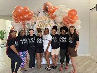 Group of seven women standing in front of a balloon decoration with pink, white, and peach balloons and a sign that says 'Scottsdale before the Veil"