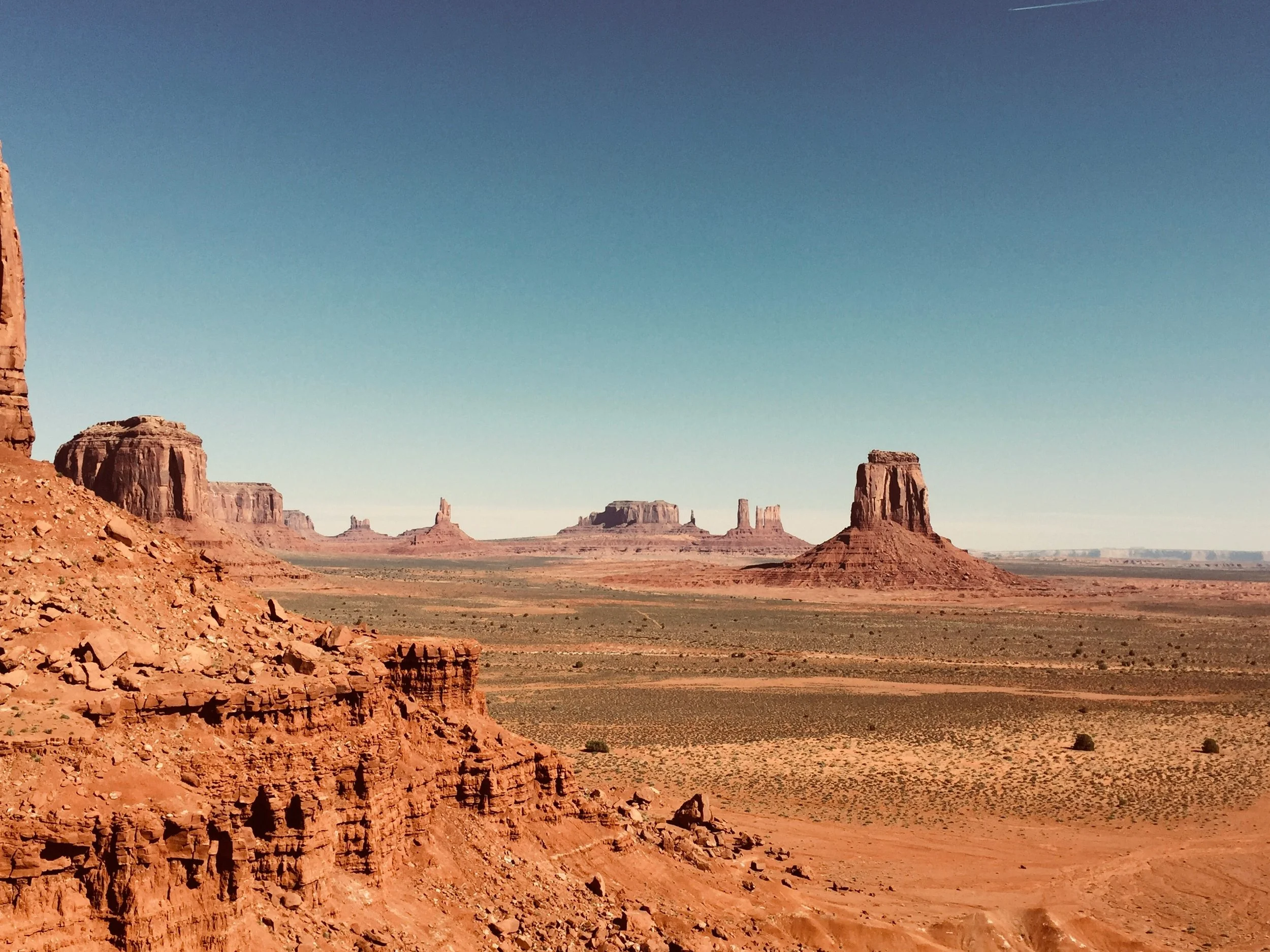 A desert landscape with large rock formations and buttes under a clear blue sky, likely Monument Valley.
