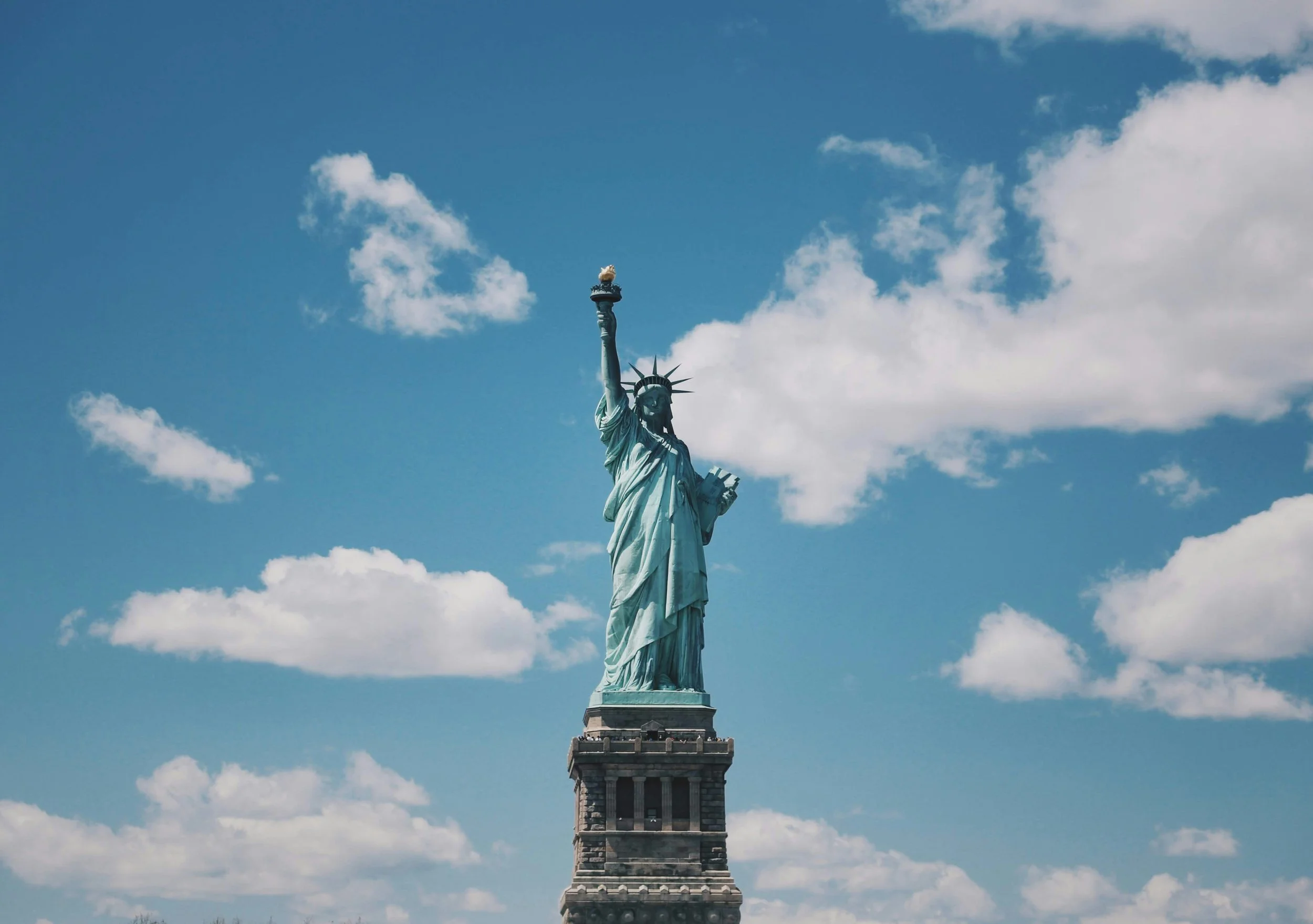 The Statue of Liberty standing tall against a blue sky with scattered clouds.