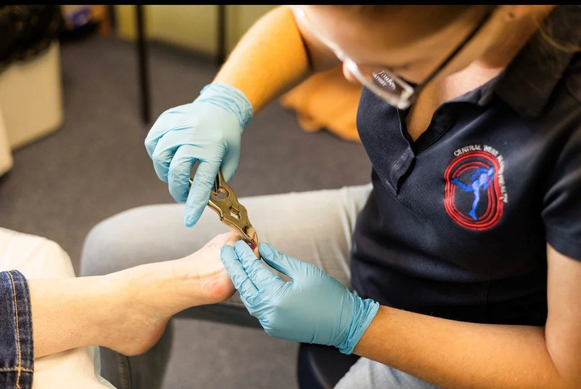 A healthcare worker wearing gloves trimming a patient's toenail with nail clippers.