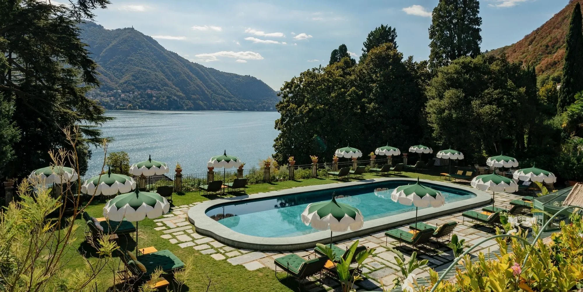 A poolside area with umbrellas and lounge chairs overlooking a lake with mountains in the background.