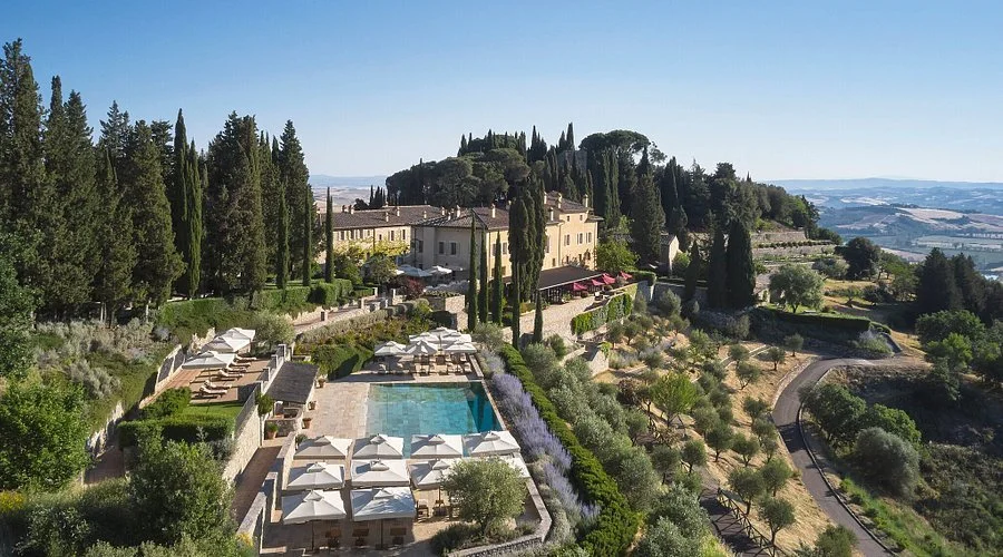 A scenic view of a luxury estate with a swimming pool, lush greenery, cypress trees, and a picturesque landscape in the background.