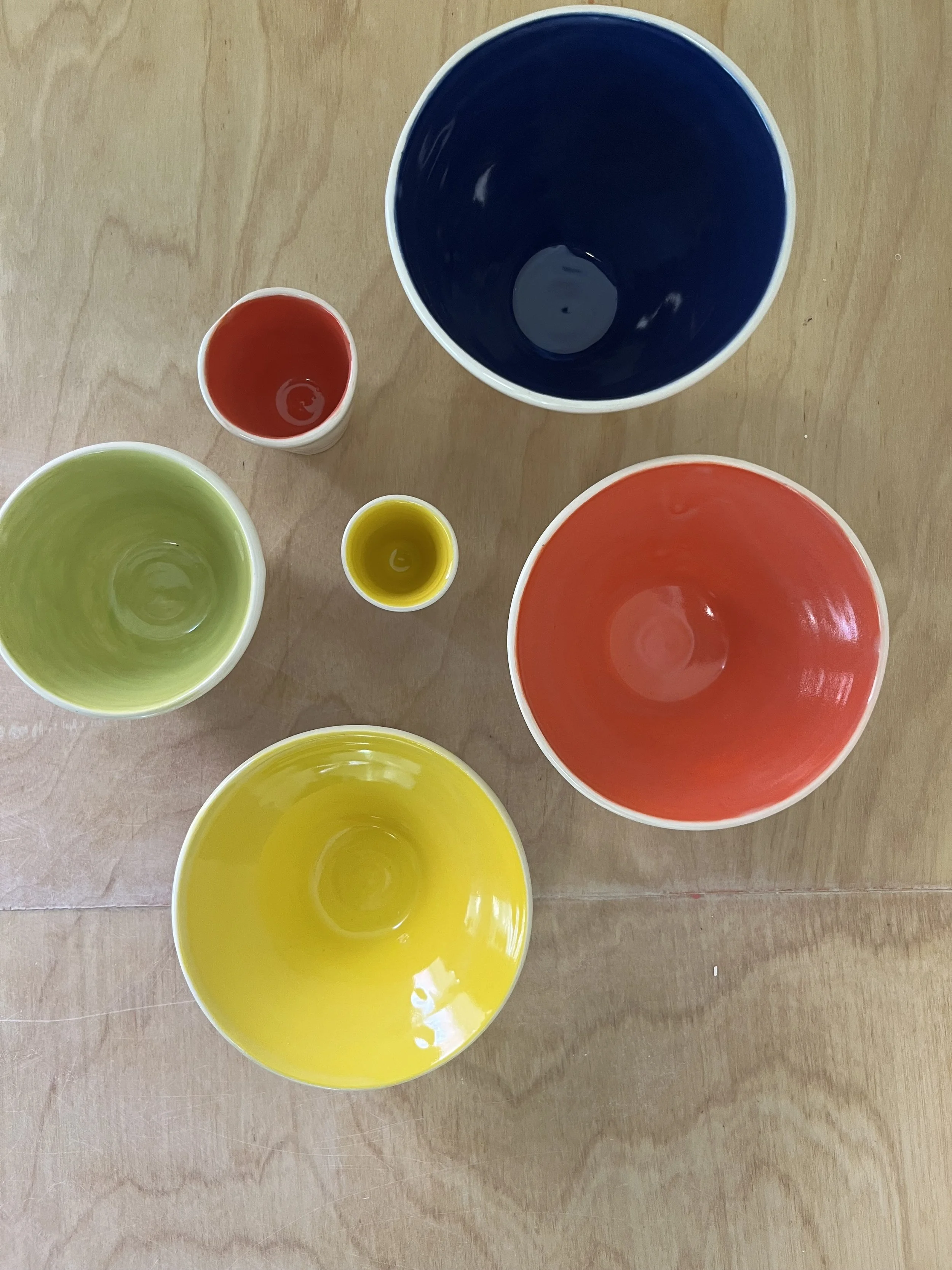 Colorful empty bowls and cups on a wooden surface, including yellow, green, red, blue, and small yellow and red cups.