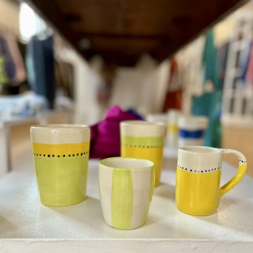 Four colorful ceramic cups with yellow, green, and white patterns on a white surface, with a blurred background.