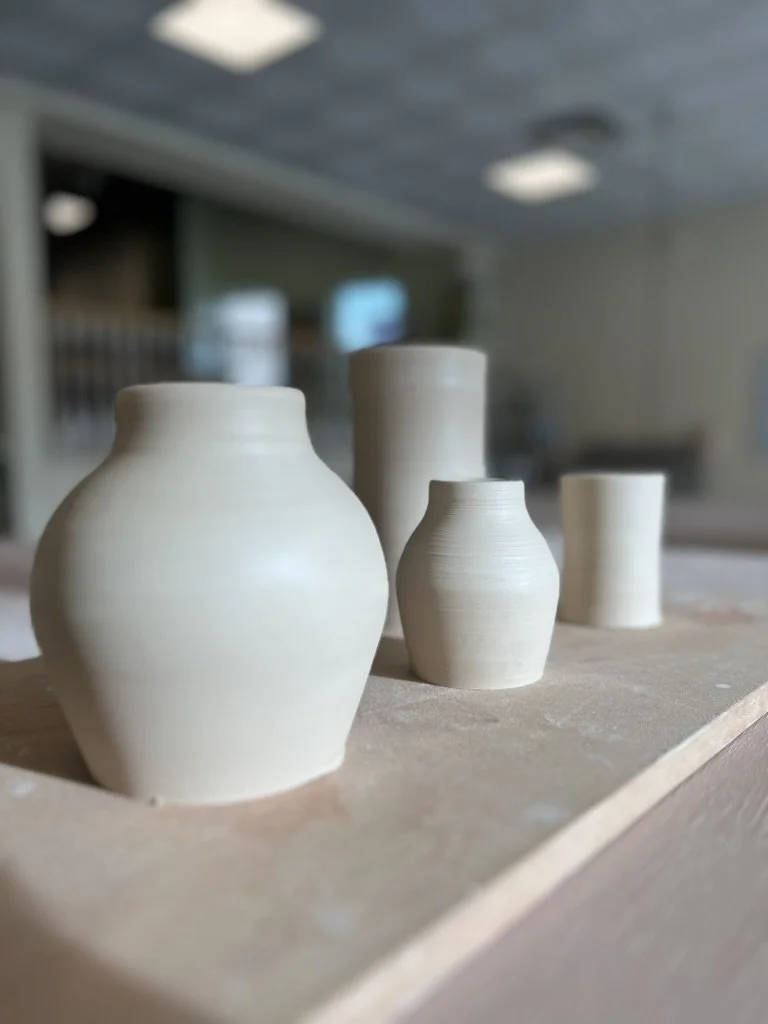 Four unglazed ceramic vases placed on a wooden work surface in a pottery studio.