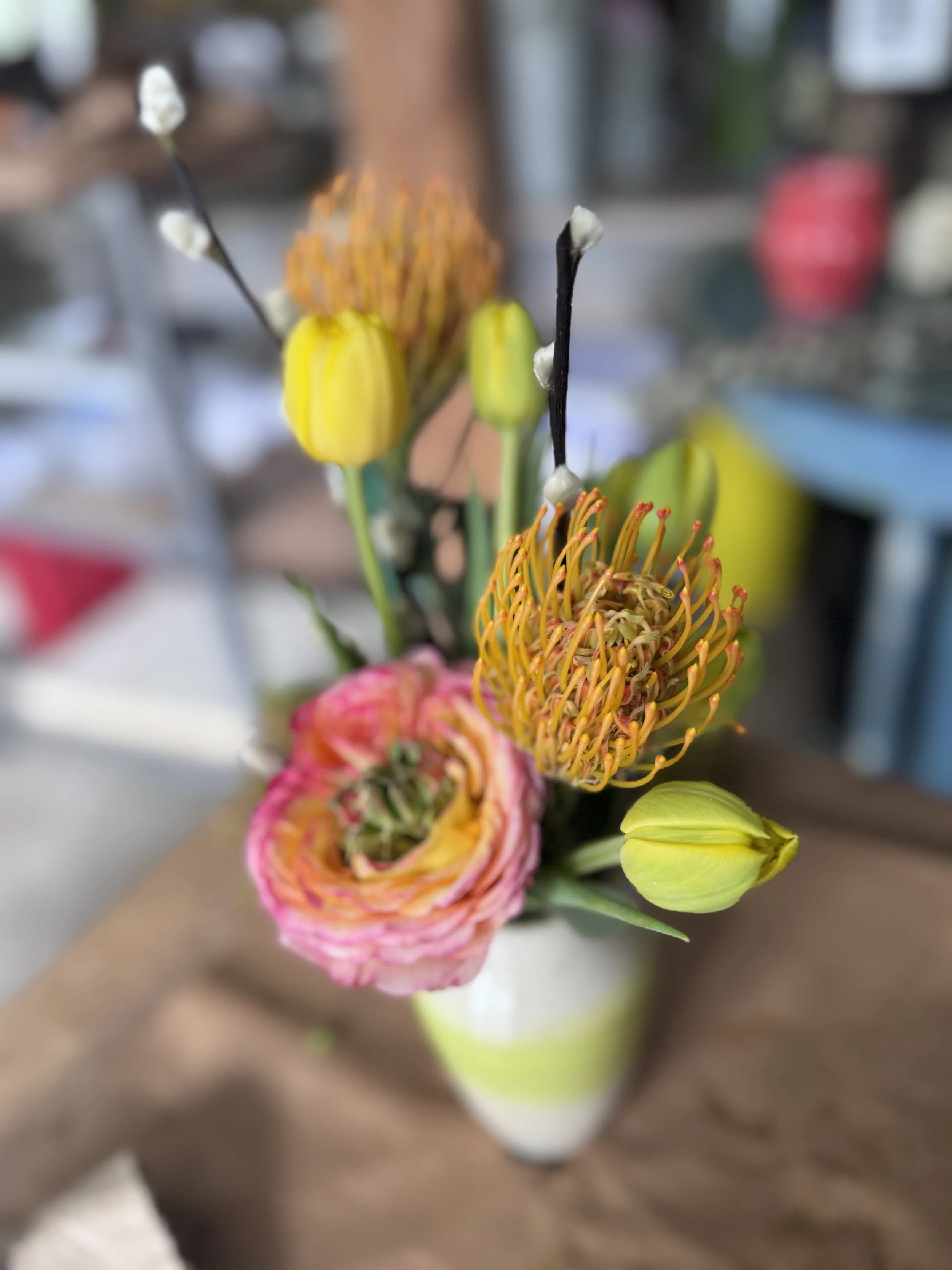Close-up of a colorful flower arrangement in a white vase with pink, yellow, and orange flowers and buds.