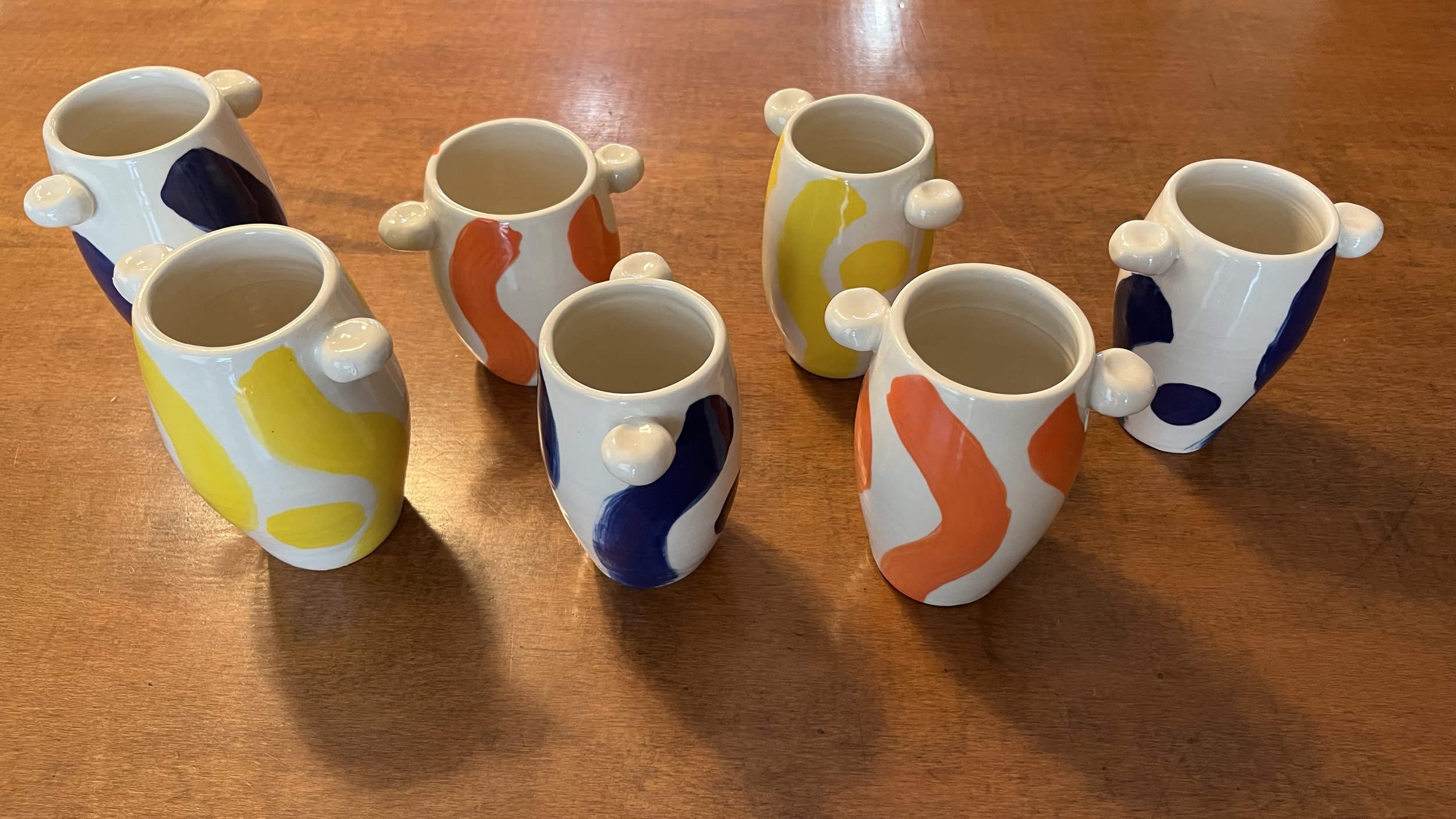 Seven small decorative vases with abstract colorful patterns on a wooden surface.
