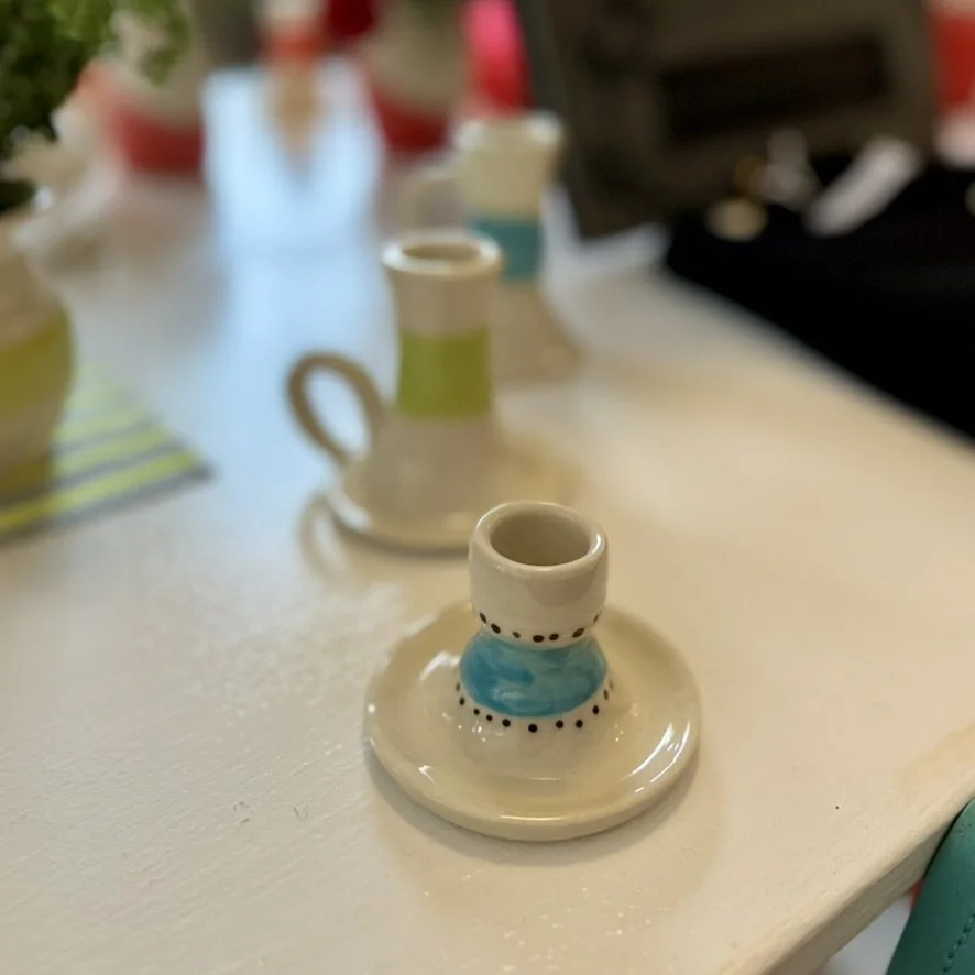 Decorative ceramic candle holder with blue and black details on a white surface, blurred background with other colorful objects.