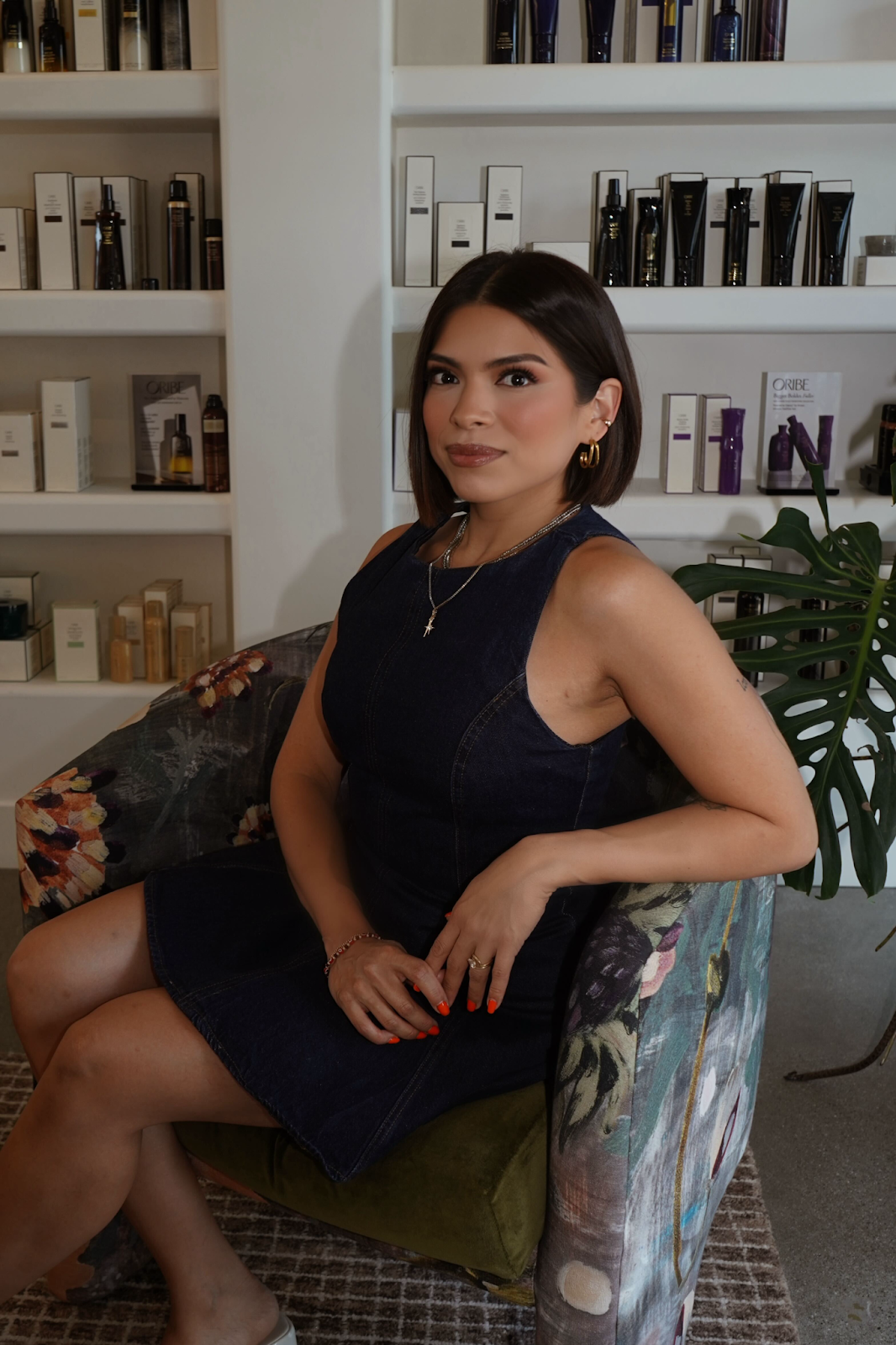 A woman sitting on an armchair in a retail or skincare store with shelves of skincare products behind her.