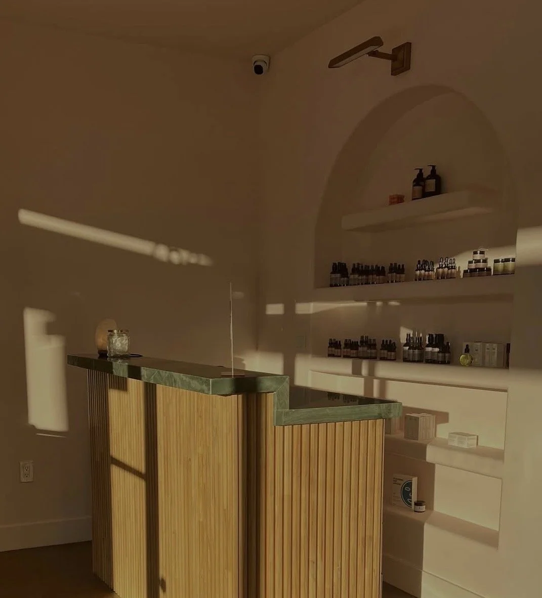 Interior of a room with a wooden counter, shelves with various bottles, and a security camera on the ceiling, illuminated by sunlight and shadows.