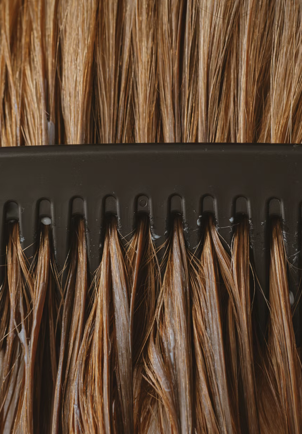 A close-up of a hair extension weft with light brown, straight hair attached to a black clip strip.