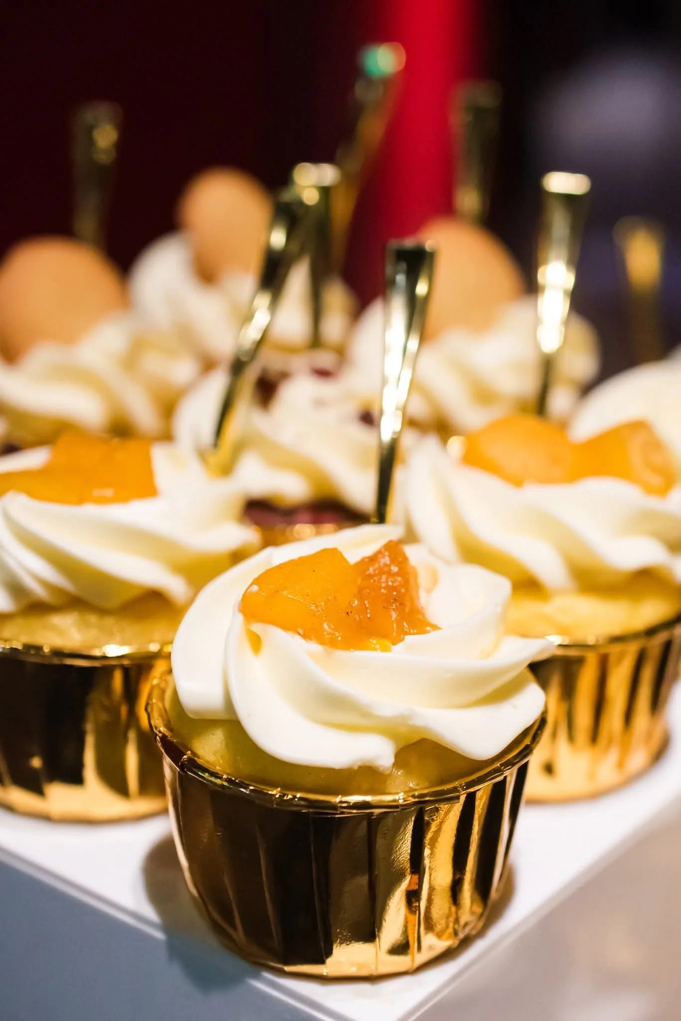 Cupcakes topped with whipped cream and an orange fruit garnish, in gold foil wrappers.