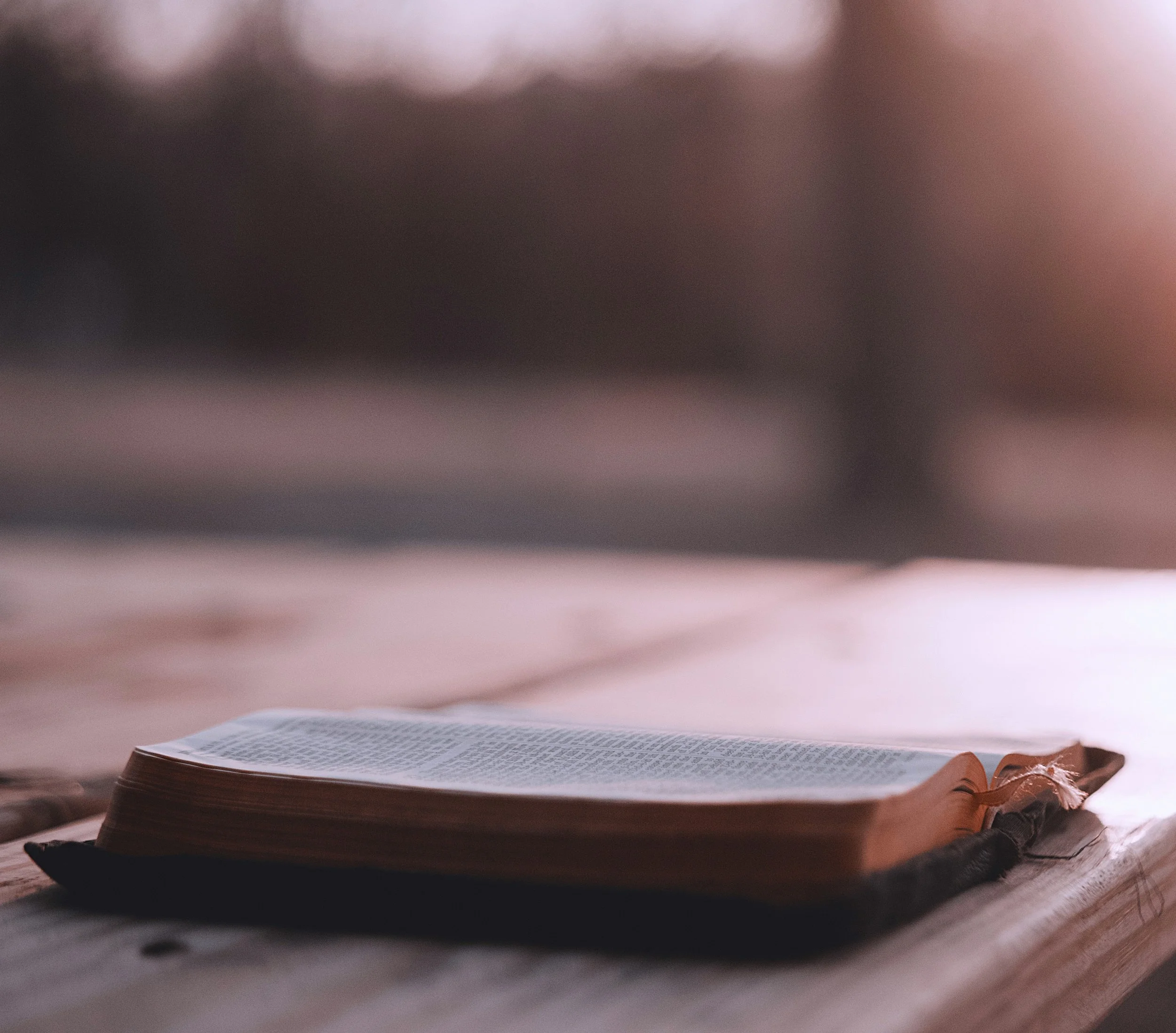 A close-up view of an open Bible laying on a flat surface, with a dark background and soft lighting.