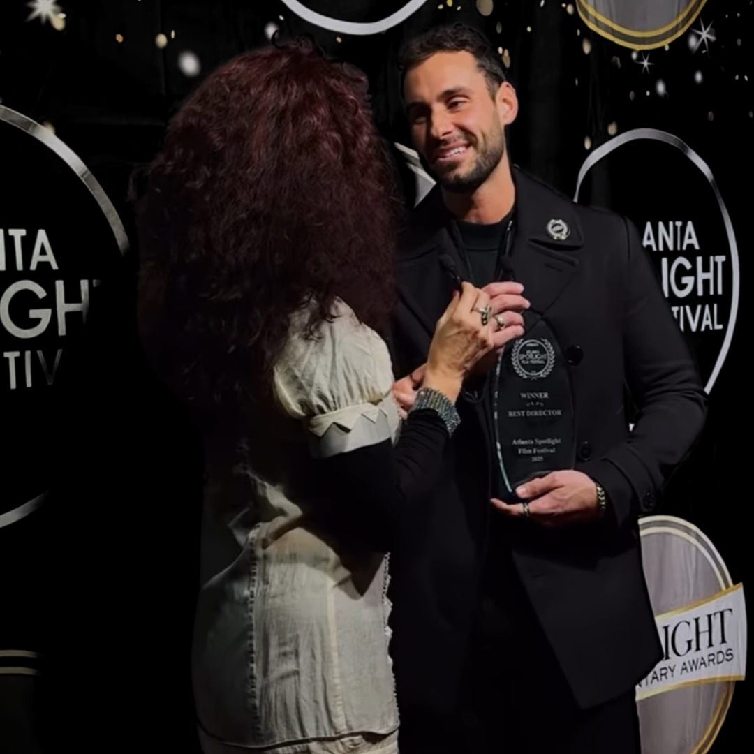 A man receiving an award from a woman at a film festival event, with a backdrop displaying the festival's name.