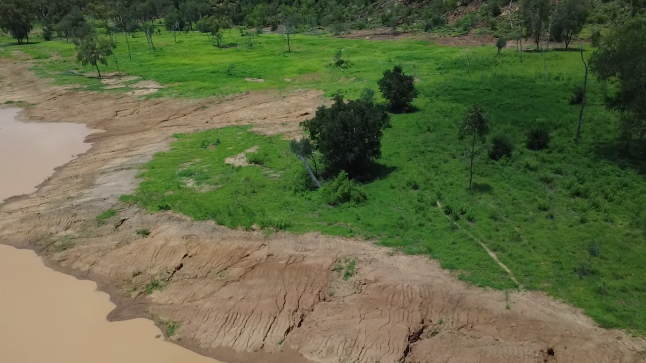 Aerial view of a partially dried riverbank with green vegetation and scattered trees.