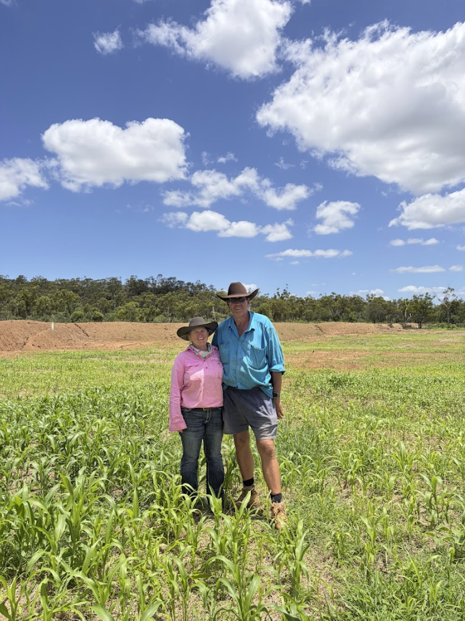 Two people standing in a field of young green crops under a blue sky with white clouds.