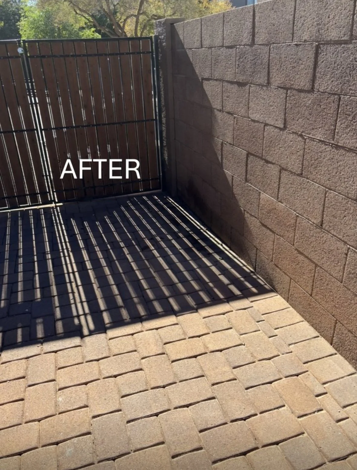 A sunlit outdoor area with a stone brick pavement, a brown wooden gate, and a beige brick wall. The word 'AFTER' is overlaid on the image, indicating a renovation or improvement.