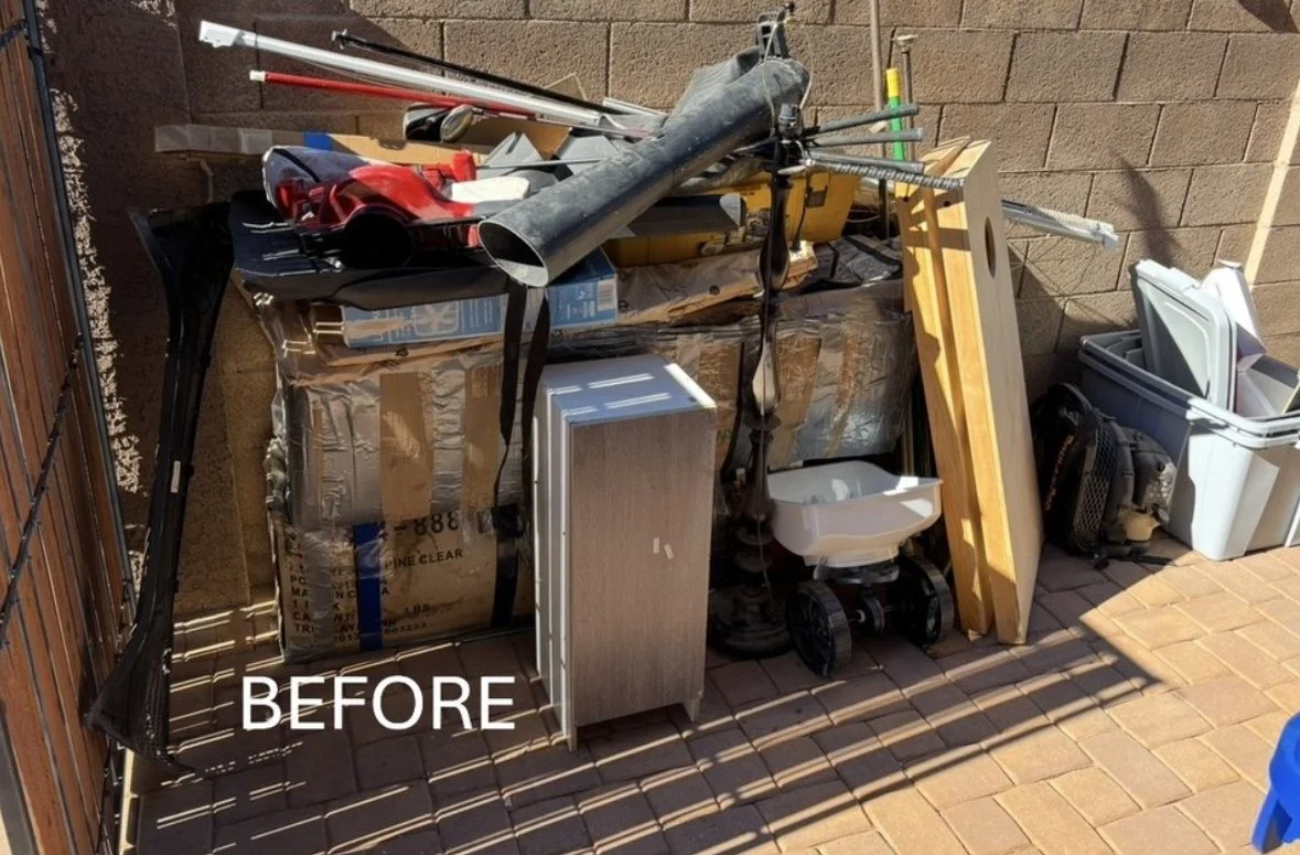 Cluttered outdoor storage area with various tools, boxes, and household items, including pipes, a small cabinet, a white plastic container, and other miscellaneous objects. The word "BEFORE" is overlaid on the image, indicating a project not started.