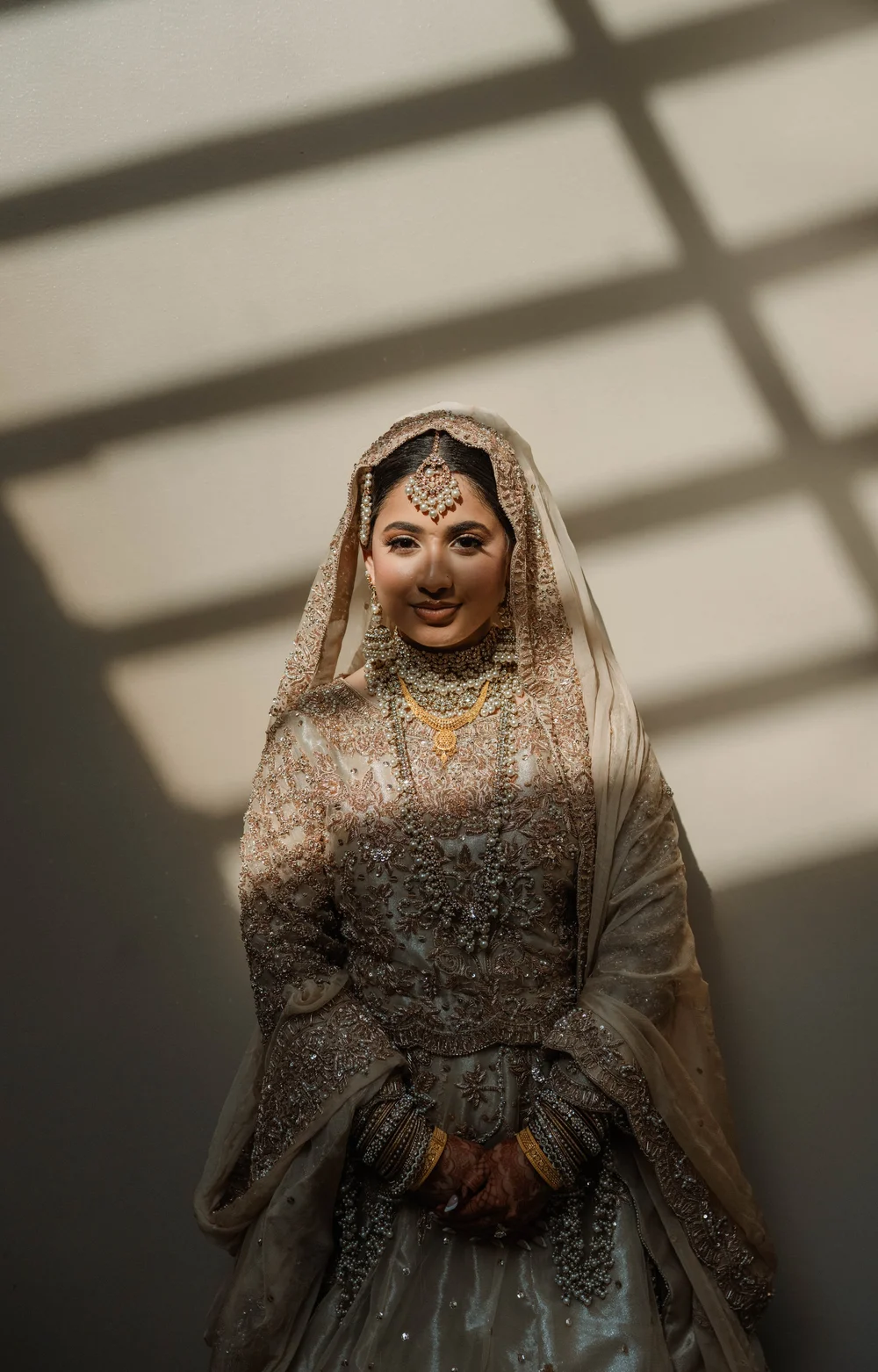 South Asian bride framed by window blind shadows