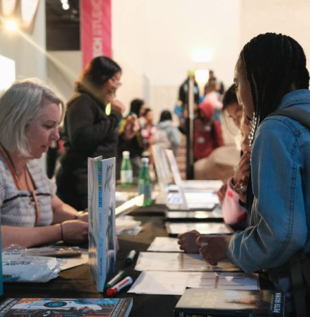 People browsing and interacting at a busy booth or table during an event or trade show.
