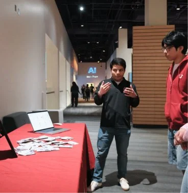 Two young men looking at display table with photos at an indoor event