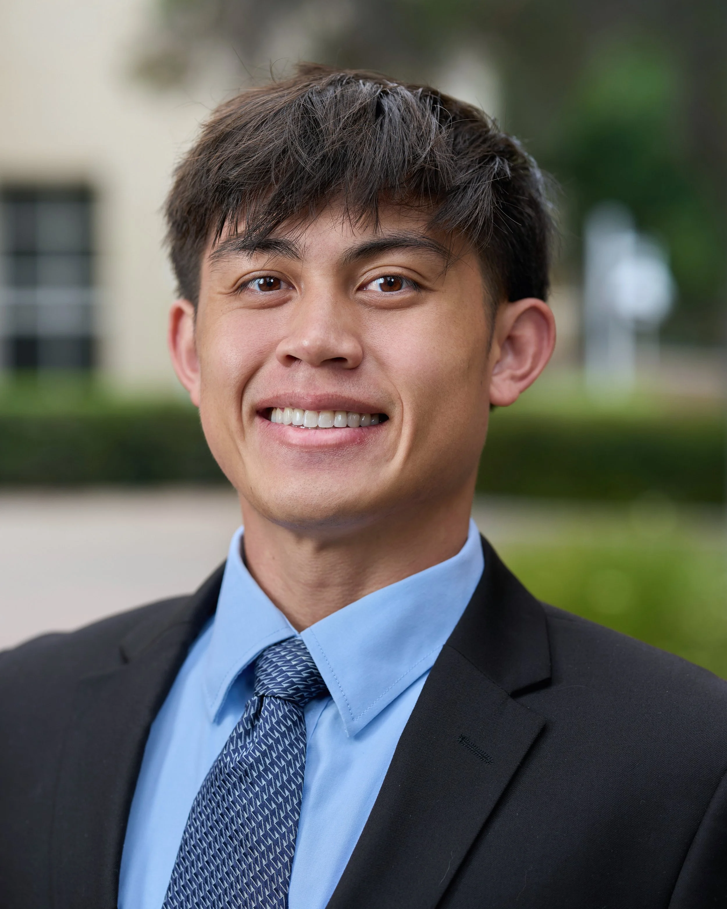 A young man in a suit and tie smiling outdoors.