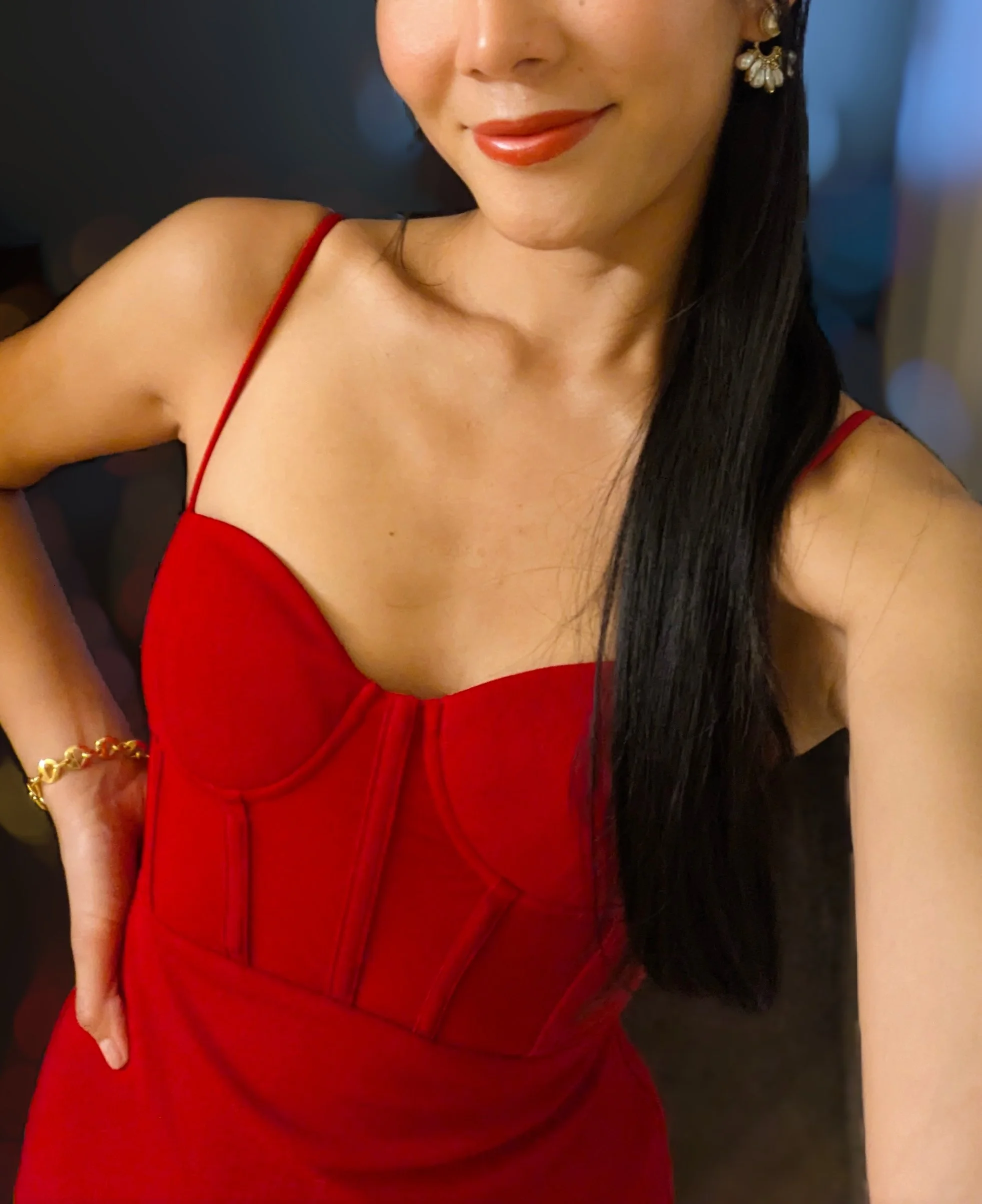 A woman wearing a red dress with thin straps, gold earrings, and a gold bracelet, smiling with dark hair and red lipstick. GFE Las Vegas, dinner date, escort, Scarlett Song Escort,