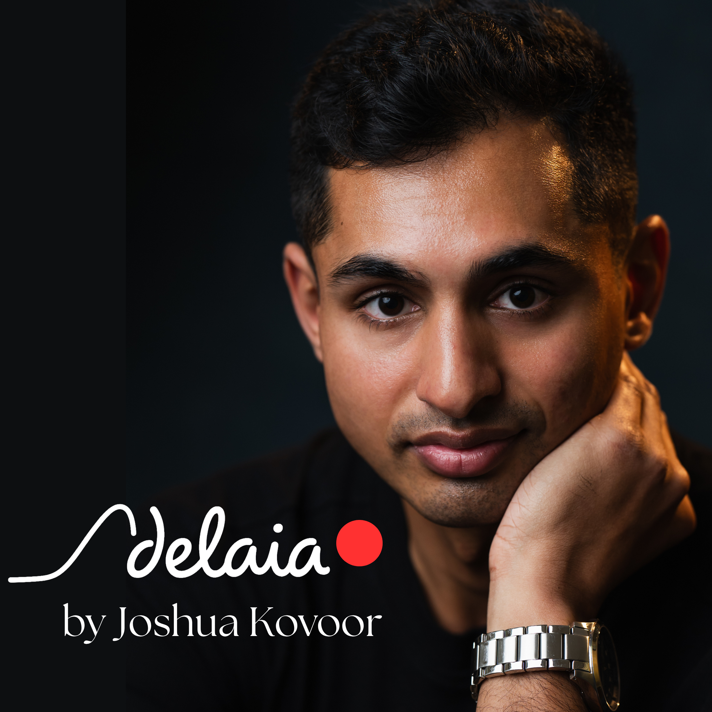 Close-up of an attractive young man with dark hair and brown eyes wearing a watch on his wrist, with the 'Adelaia by Joshua Kovoor' visible in the foreground.