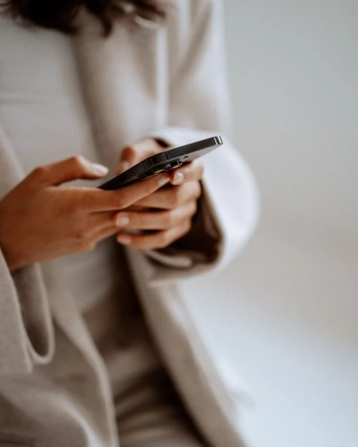 A person wearing a beige jacket holding and using a smartphone