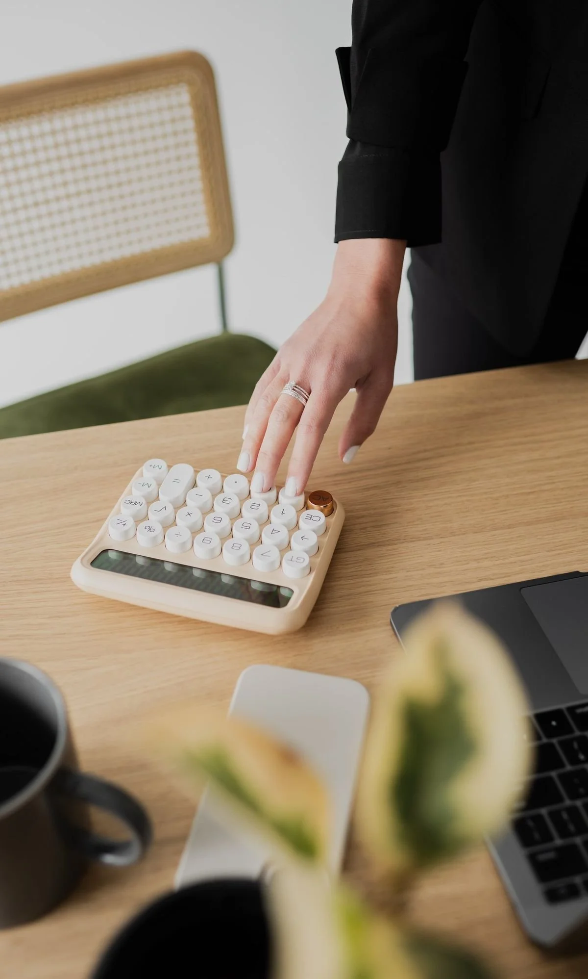 Person in black shirt using a creative calculator with round white buttons on a wooden desk.