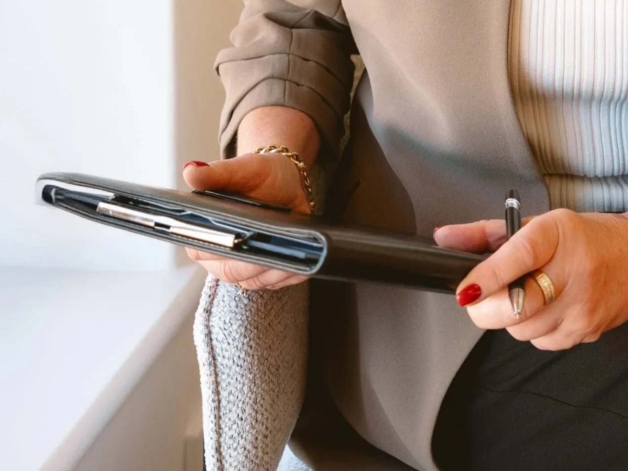 Stack of four binders filled with papers beside a white coffee cup on a saucer on a desk.