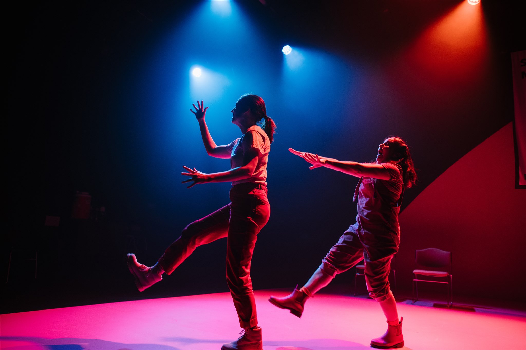 Two performers dancing on stage under colorful lights with a purple-pink stage floor.
