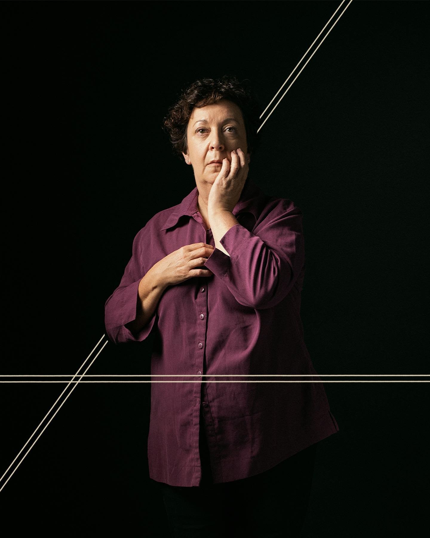 A woman in a purple shirt holding her face with one hand, with a pensive expression, against a black background decorated with white linear designs.