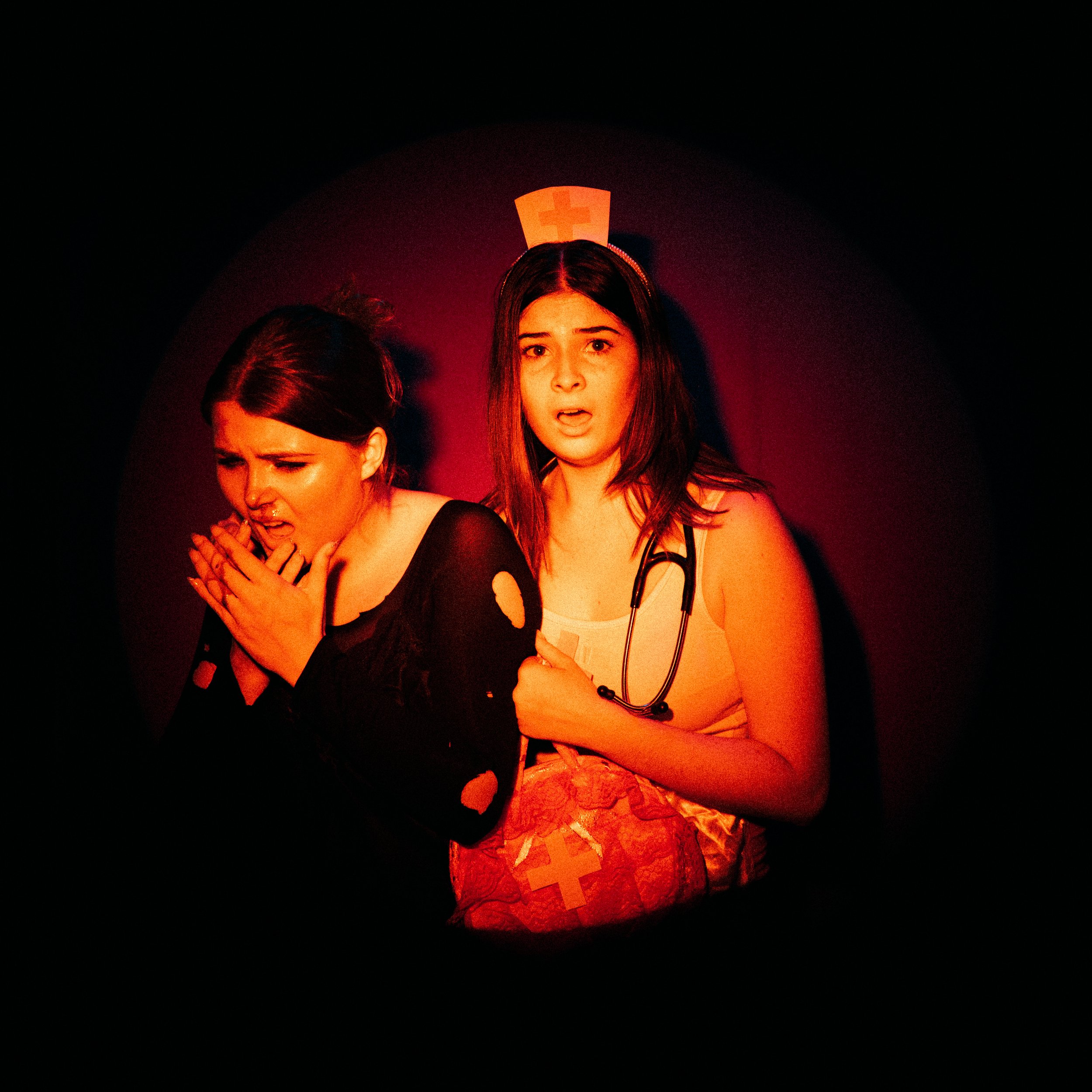 Two women, one a nurse and one a patient, in distress in a dark room with a red glow, a nurse's white cross hat in the background.