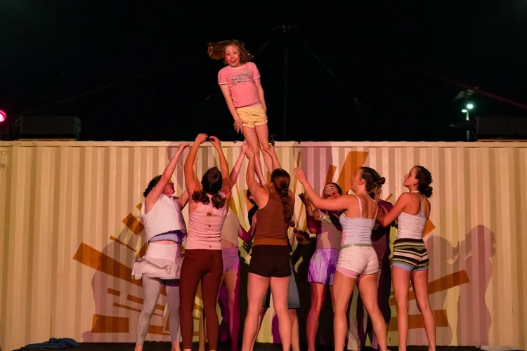 A group of young girls performing a cheerleading stunt outdoors at night, with one girl lifted above the others.