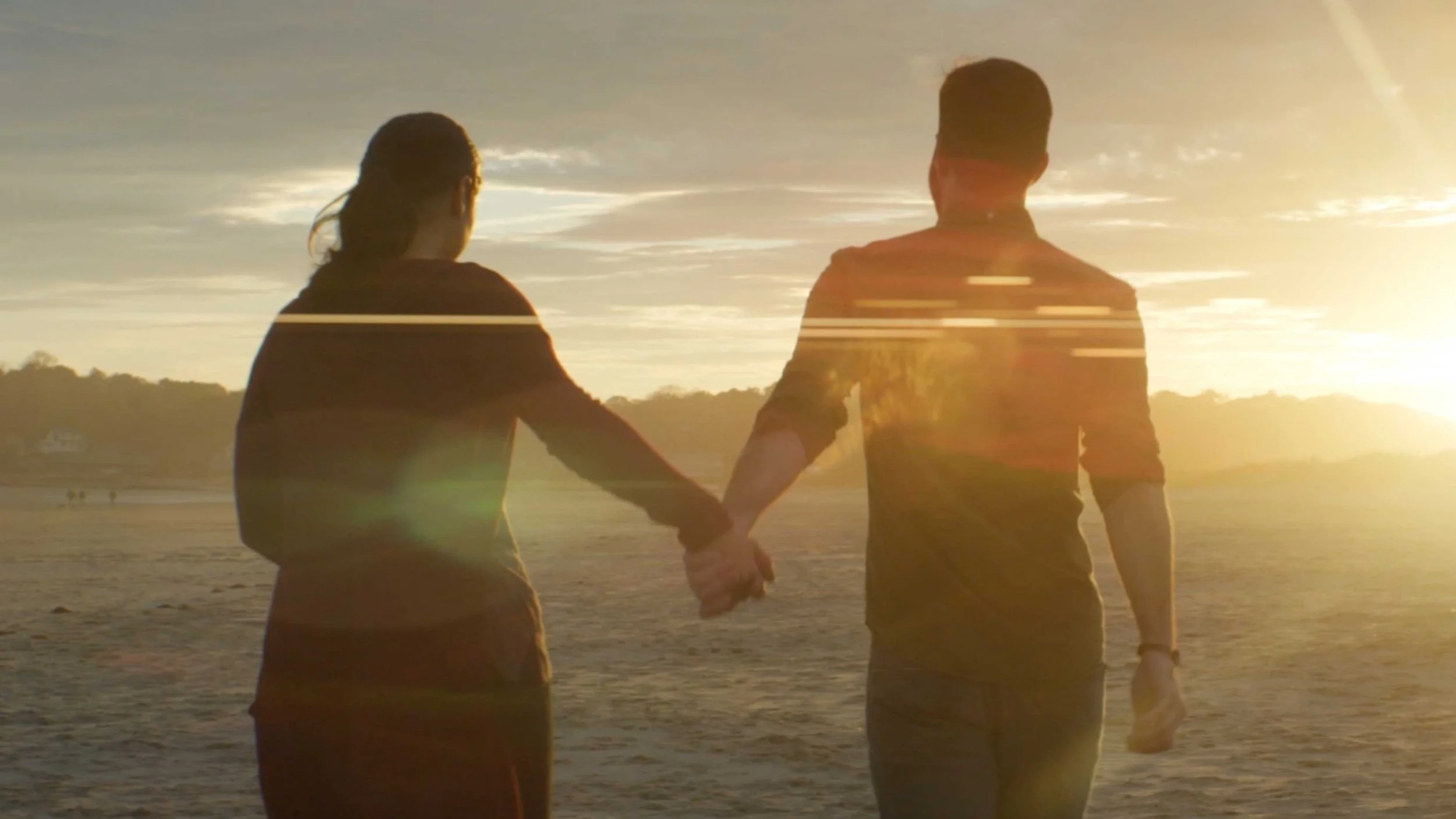 A man and woman walk hand in hand on a beach at sunset in A.W. Hastings future vision brand video for an industry event