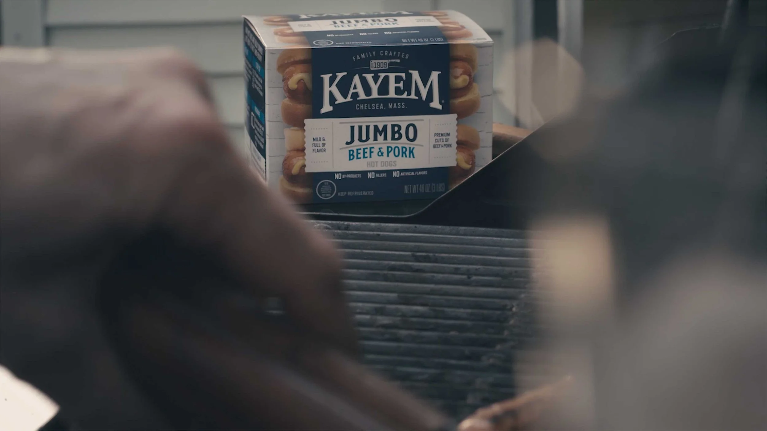 A box of Kayem hotdogs sits next to a grill for a Kayem tv ad video