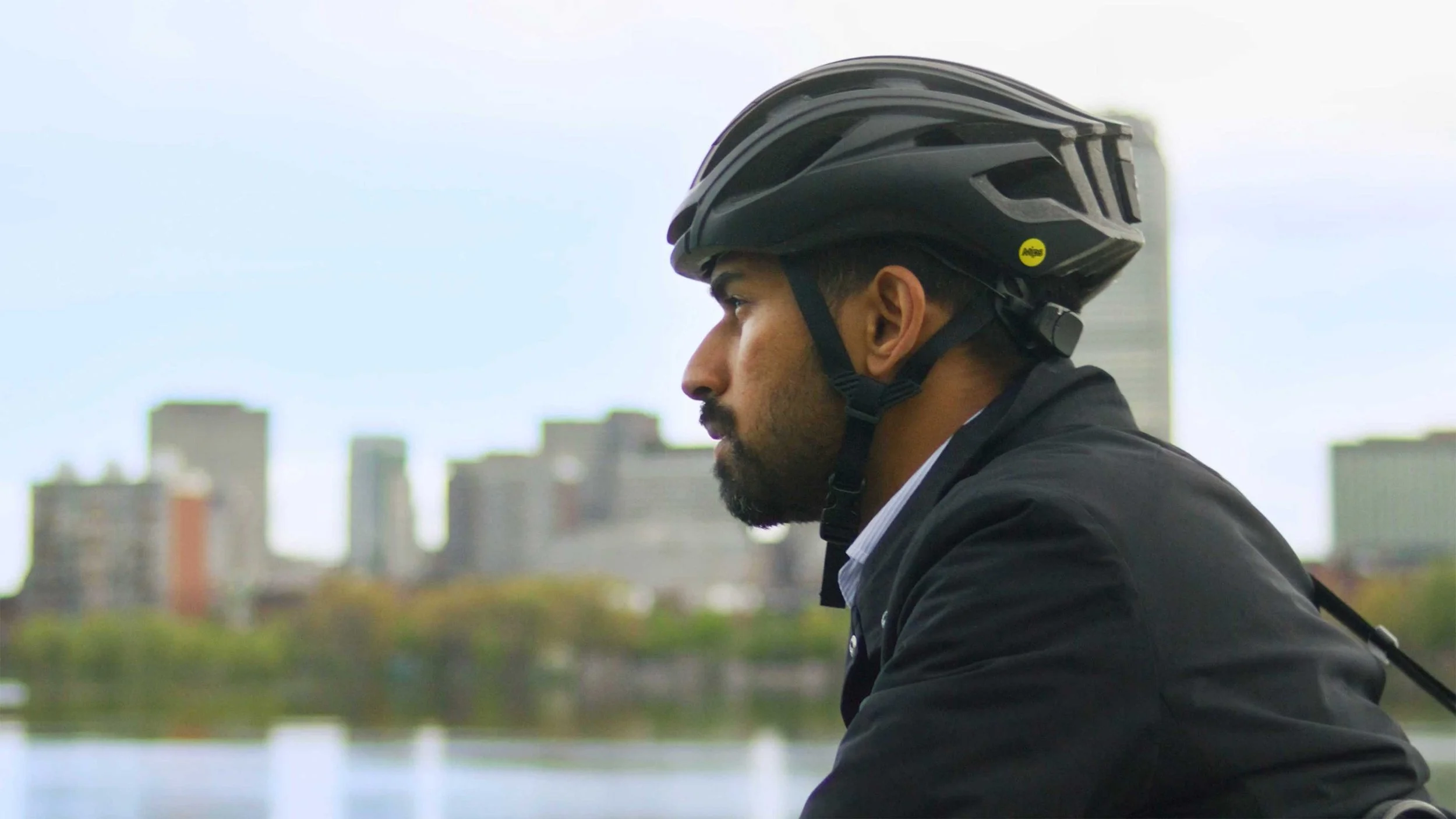 A man rides a bicycle in front of the Boston skyline in a documentary video for Ministry of Supply